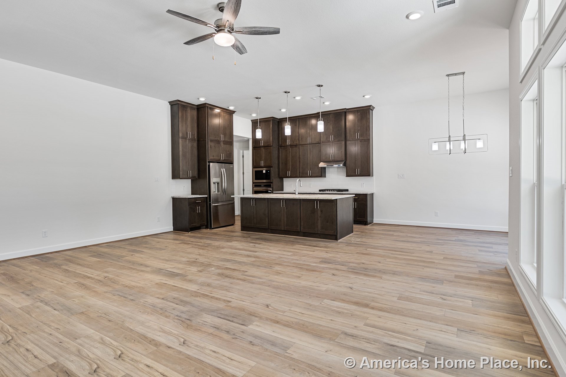 Spacious open kitchen with dark wood cabinetry, quartz island countertop, stainless steel appliances, wide plank wood flooring, pendant and recessed lighting, built-in oven, range
