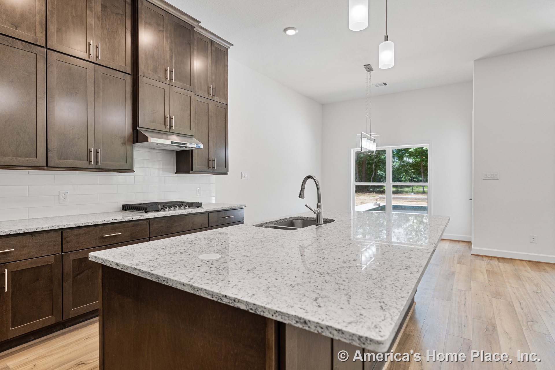 Dark wood cabinetry and full-height upper cabinets frame a spacious kitchen with granite countertops, a large island featuring an undermount sink, built-in gas cooktop with
