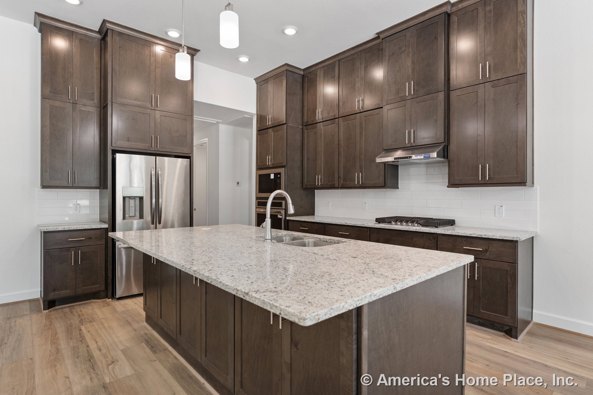 Dark wood cabinetry with tall upper cabinets, granite countertops and large central island, stainless steel refrigerator, built-in oven and microwave, gas cooktop, subway tile