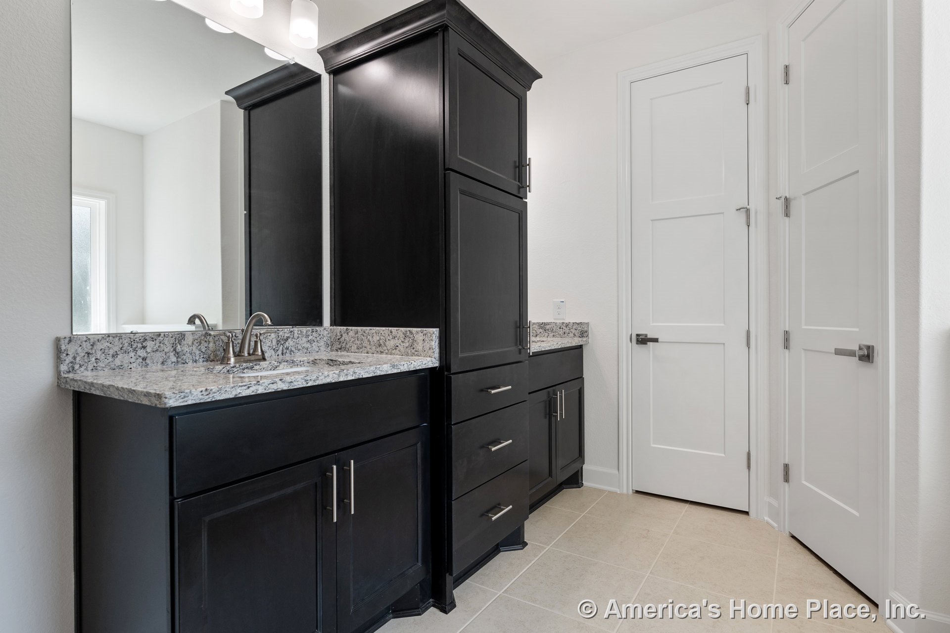 Dark wood cabinetry with granite countertops, large wall mirror above built-in vanity with integrated lighting, tile flooring, white paneled doors, and chrome sink faucet.