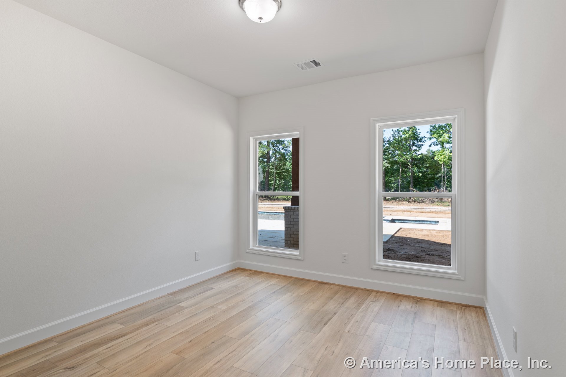 Small room with light wood plank flooring, white painted walls, two large windows with white trim, baseboard molding, and a flush mount ceiling light.