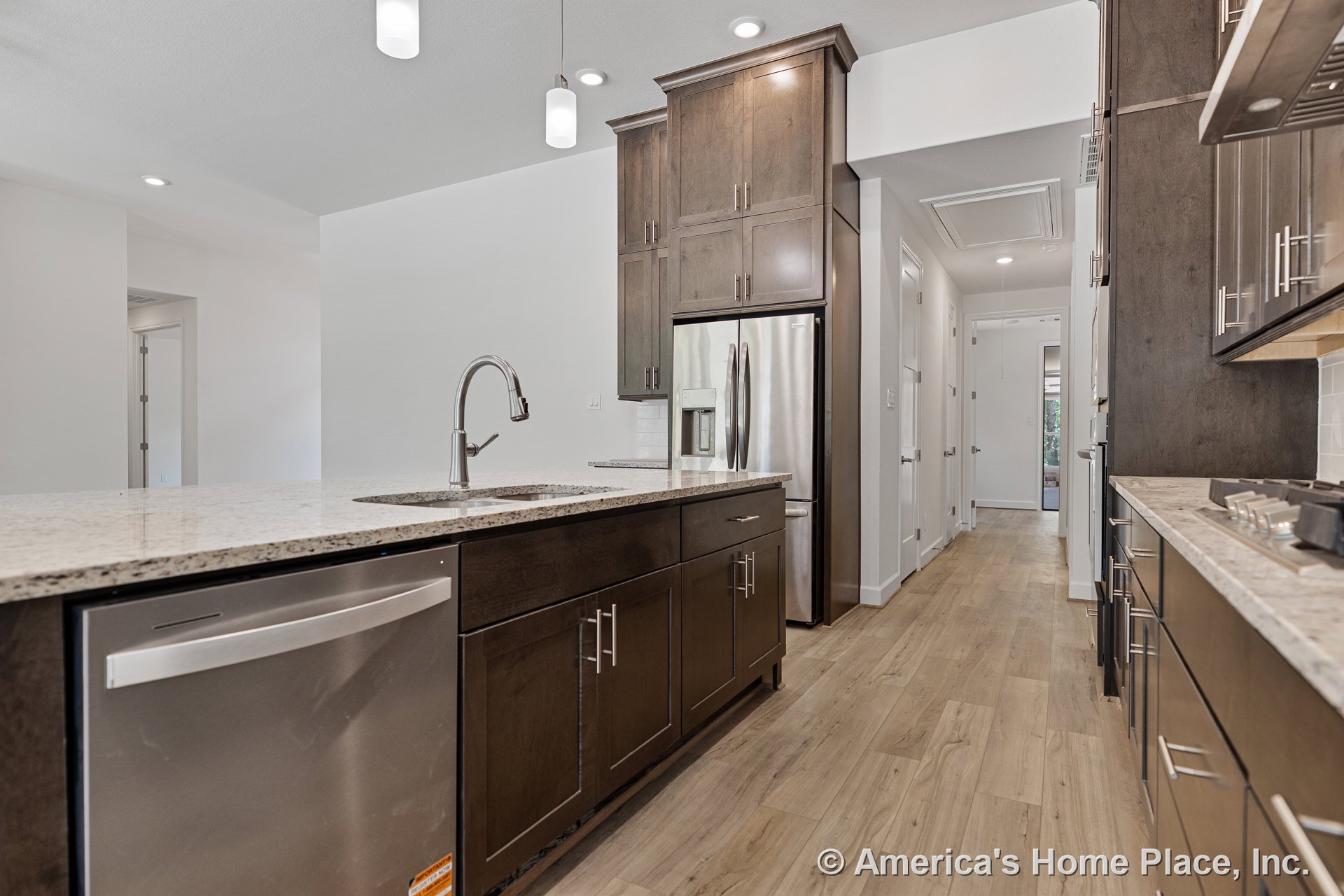 Dark wood cabinetry, granite countertops, stainless steel refrigerator, built-in dishwasher, pendant lighting, and light wood flooring in a modern kitchen with sleek fixtures.
