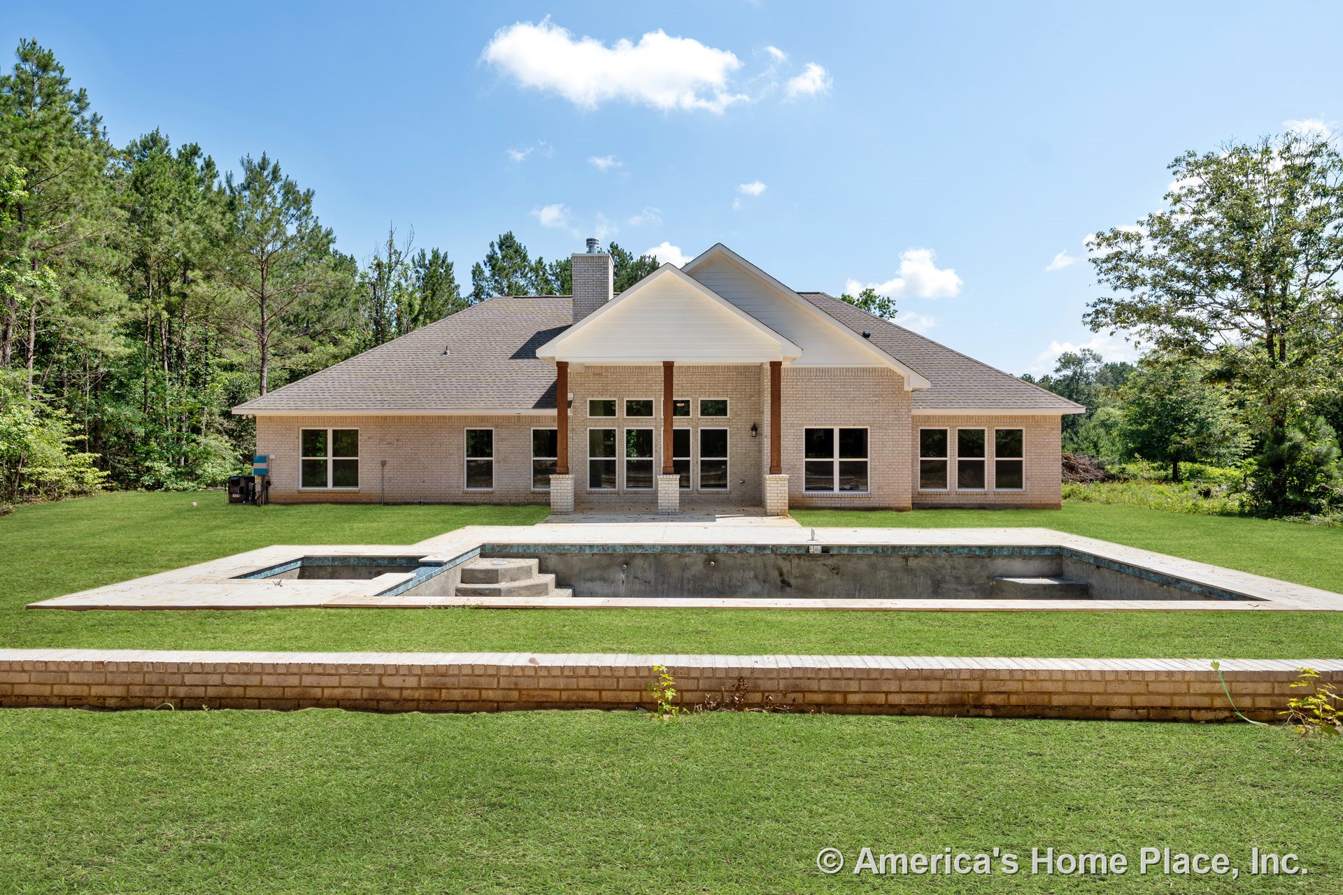 Covered rear porch with brick columns, multiple large windows, brick exterior walls, hip shingle roof, unfinished in-ground pool, and rear yard with retaining wall.