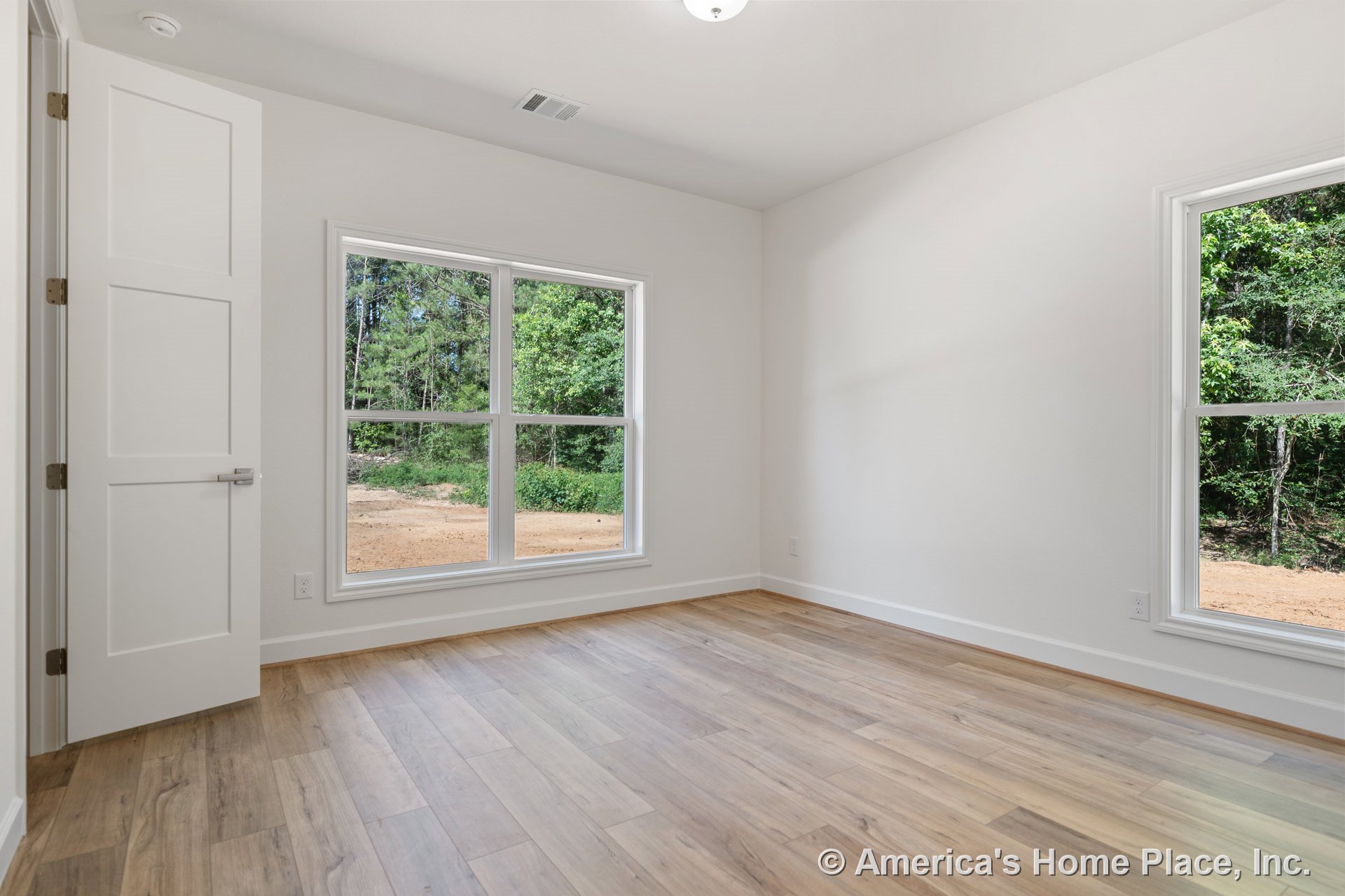 Large double-pane windows with white trim and baseboards, paneled interior door, recessed ceiling light, neutral wall color, and wood-look plank flooring in a bright minimalist
