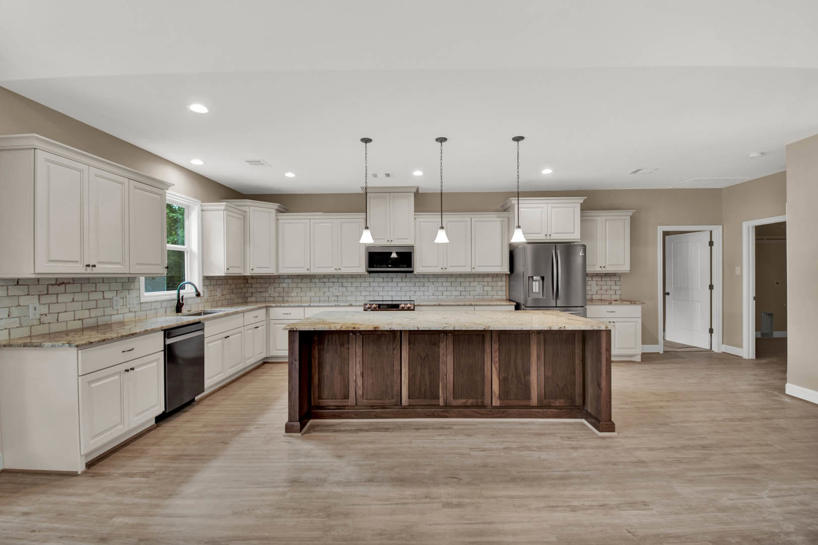 Spacious kitchen featuring a large central island with stone countertop, tile flooring, white cabinetry, stainless steel appliances including refrigerator and microwave, and a deep