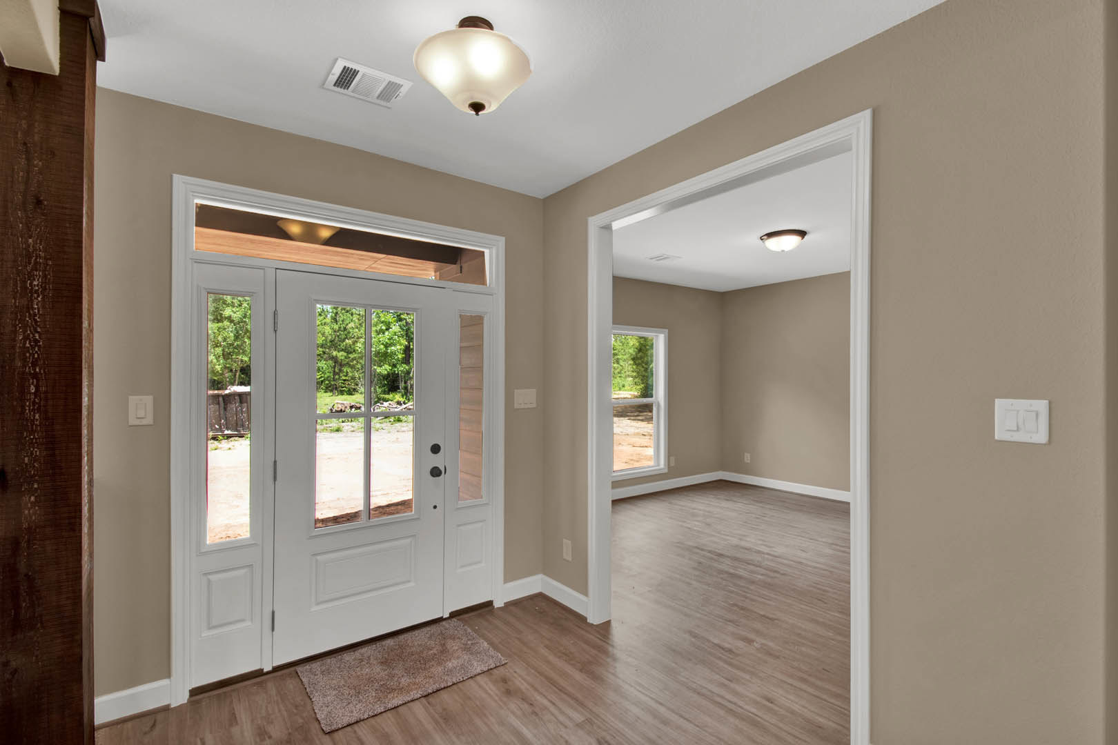Hallway with wood flooring and brown carpet, white door with glass panels, dark brown accent wall, modern light fixture, and dual white light switch