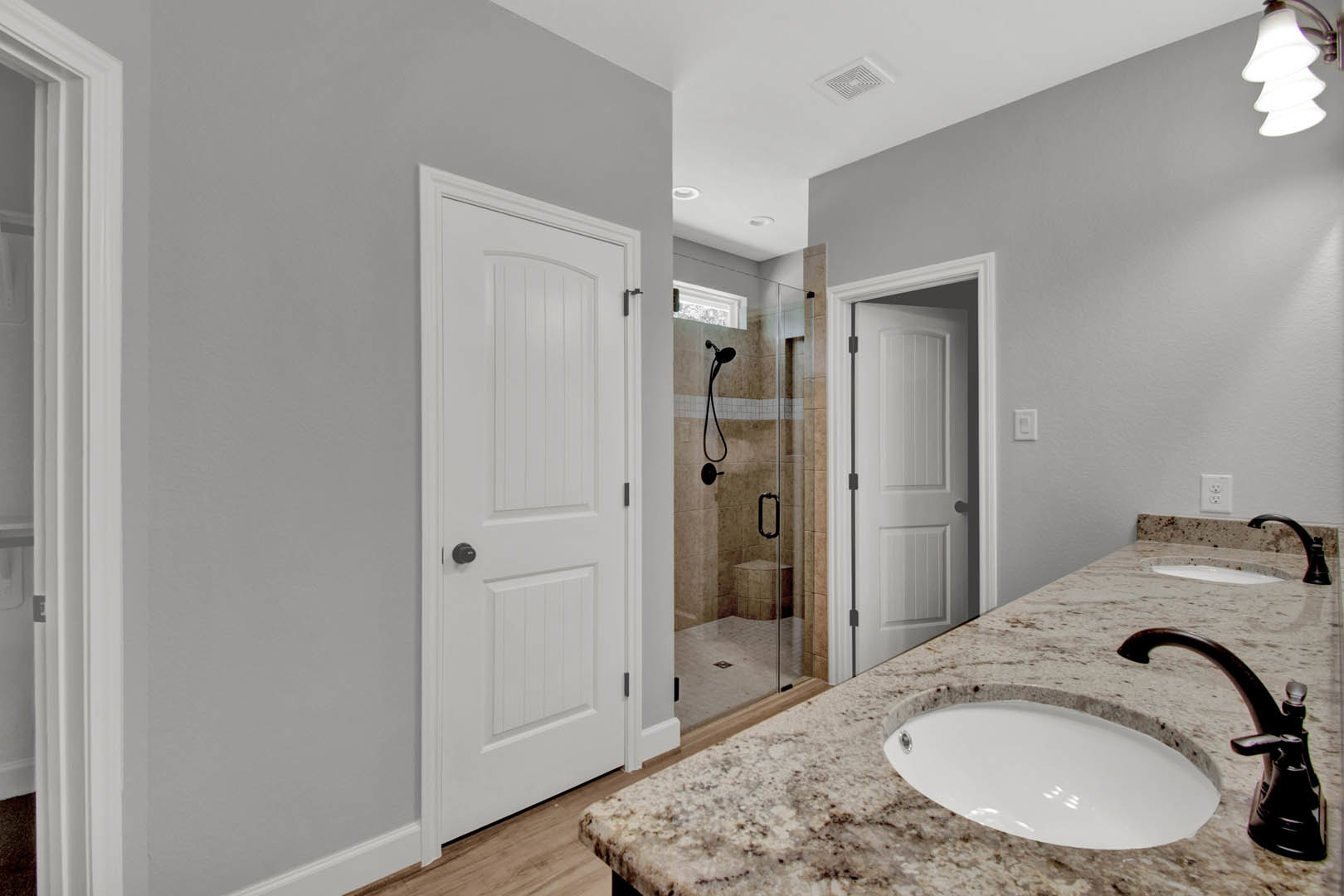 Bathroom with marble countertop, undermount white sink, glass-enclosed tile shower, wall-mounted mirror, and white door with black handle