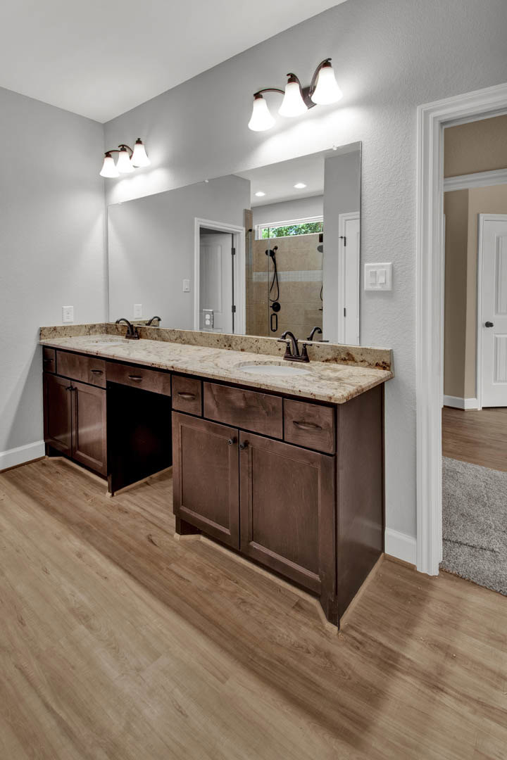Double vanity bathroom with marble countertop, three-light fixture above mirrors, wood floor, white cabinetry with black handles, and white door with black hardware.