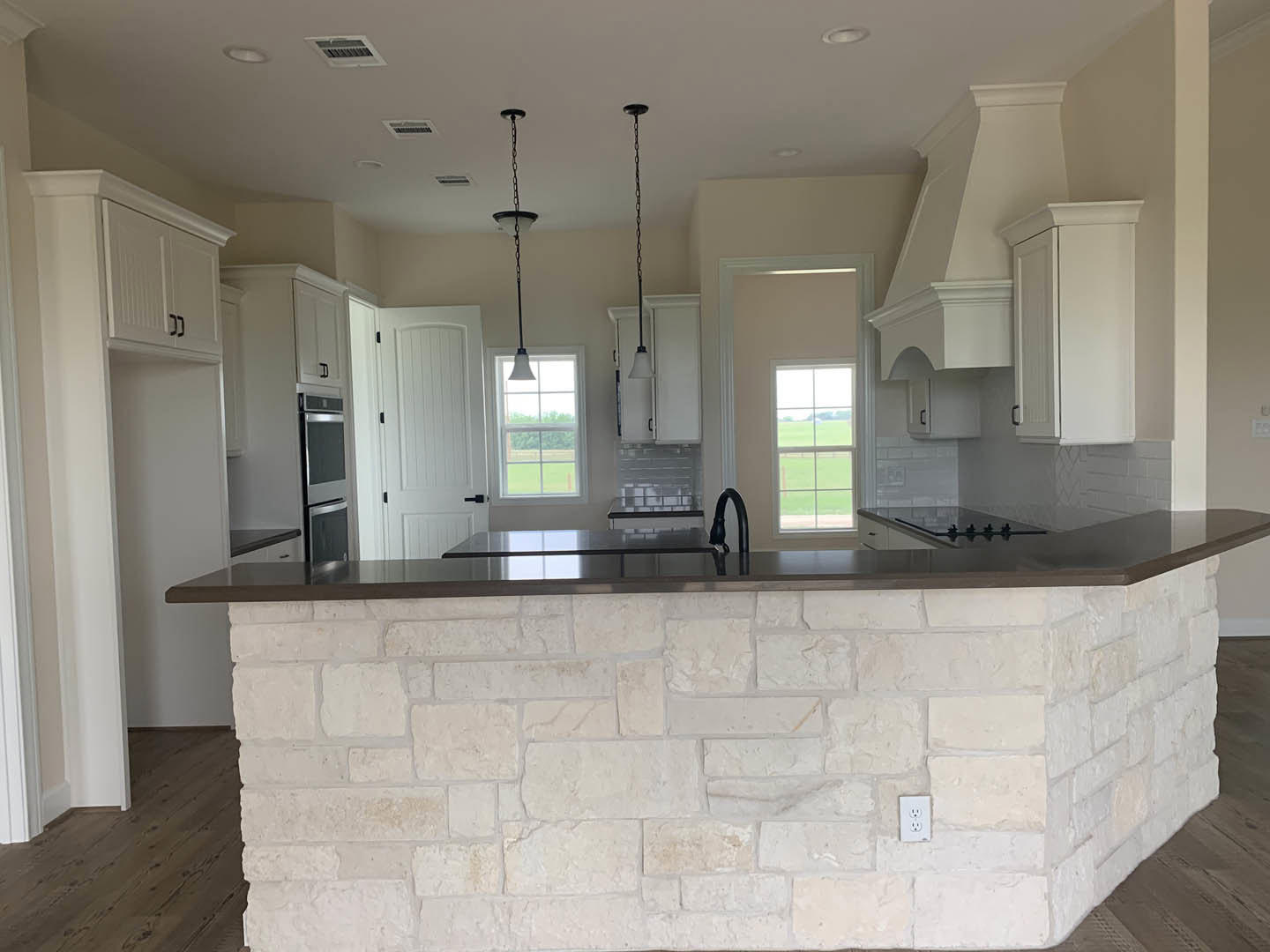 Kitchen featuring a granite island, stone accent wall with black sink and faucet, stainless refrigerator, large window overlooking a field, and light streaming through the window.
