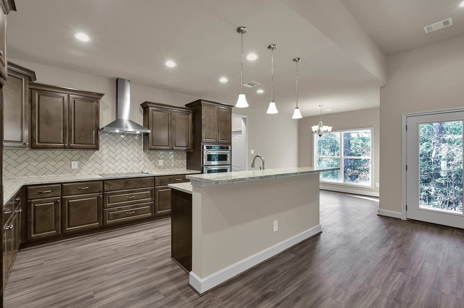 Open kitchen with marble countertops, wood flooring, stainless steel oven, white cabinetry, bar seating, and large window overlooking trees