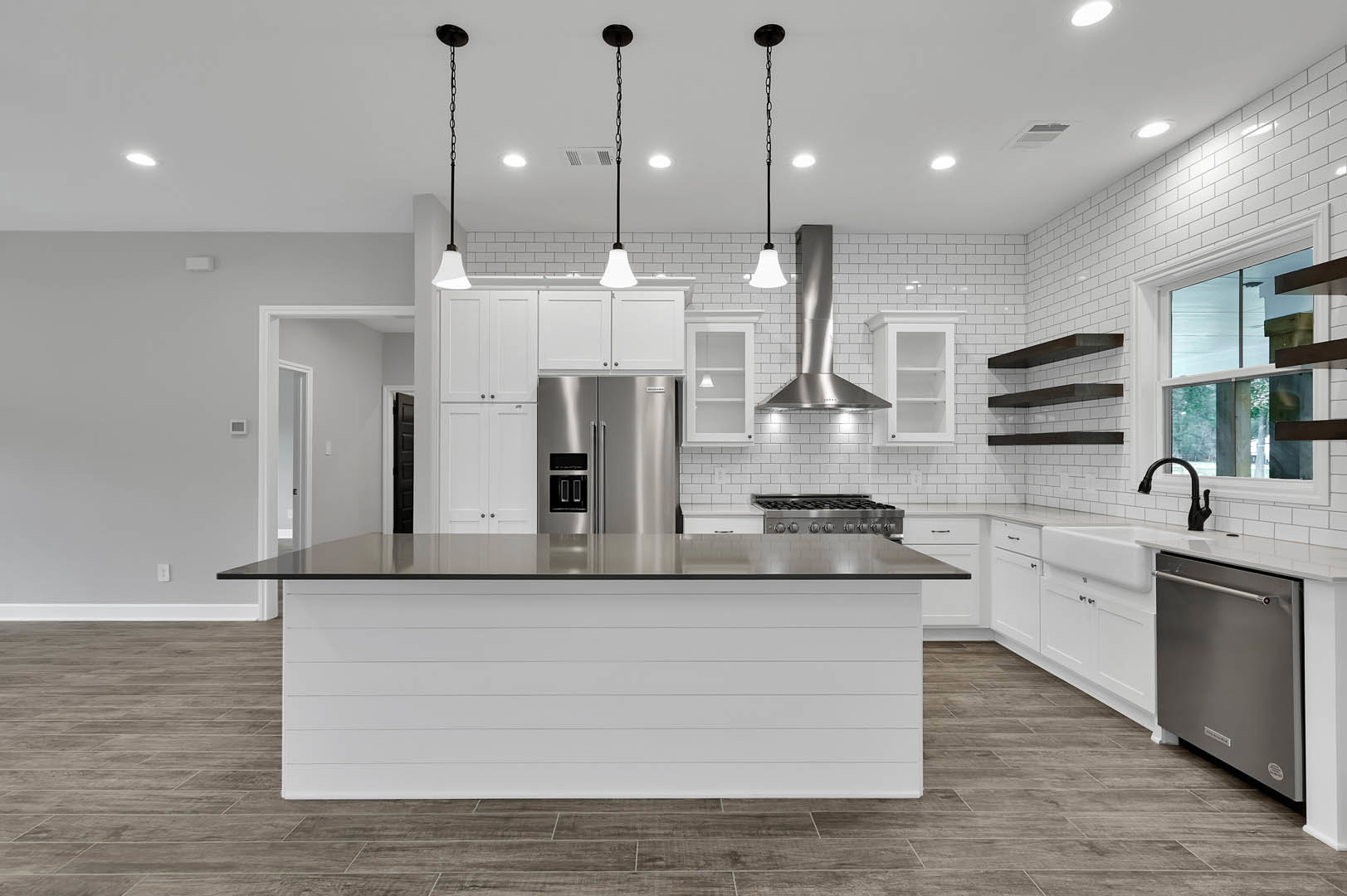 White kitchen featuring a large island with black countertop, stainless steel refrigerator and dishwasher, cabinetry, sink, and a black pendant lamp with chain above the island