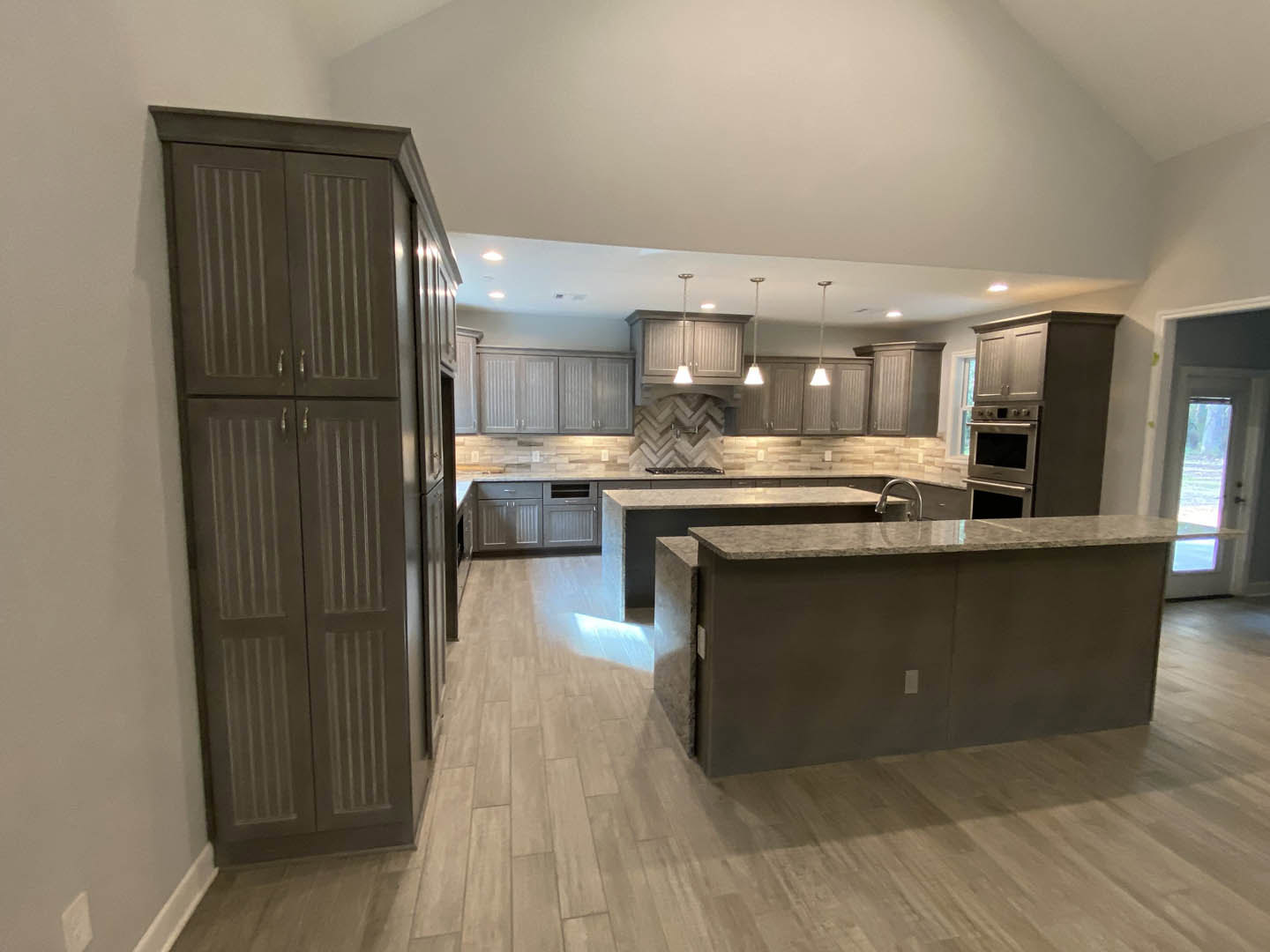 Spacious kitchen featuring a large central island with stone countertop, white cabinetry, stainless steel sink and faucet, tile backsplash, and built-in stove and oven.