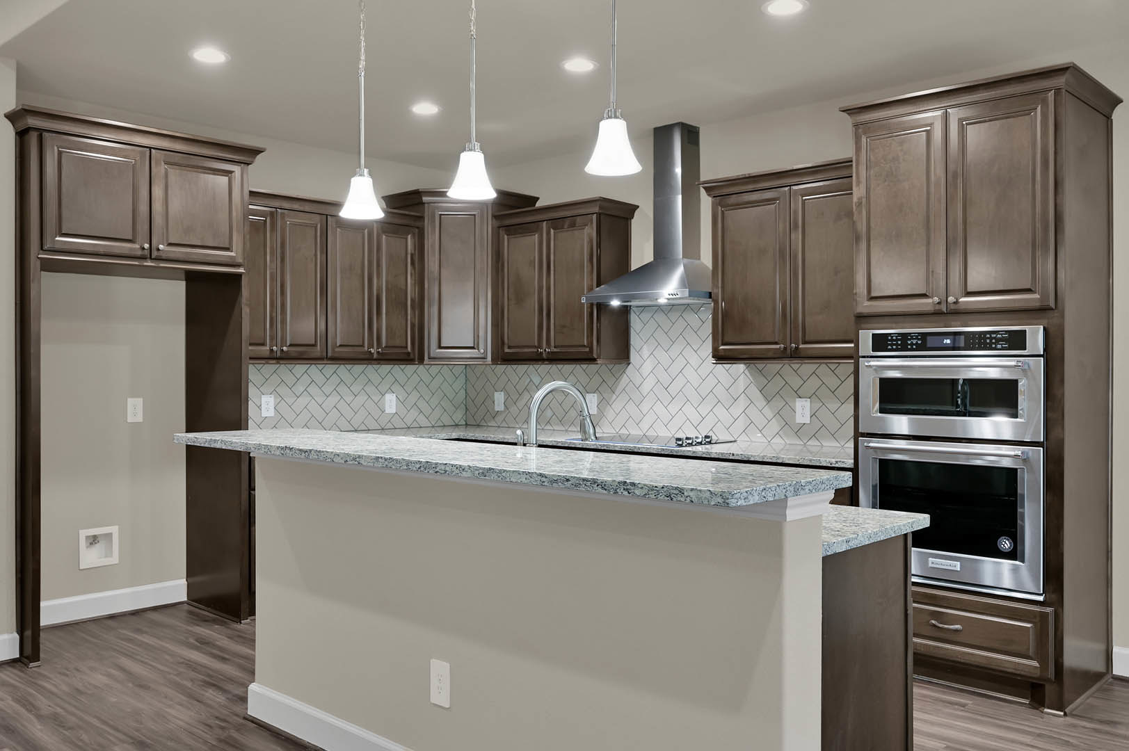 Marble kitchen island with undermount sink, stainless steel oven and refrigerator, white cabinetry, pendant light fixture above counter