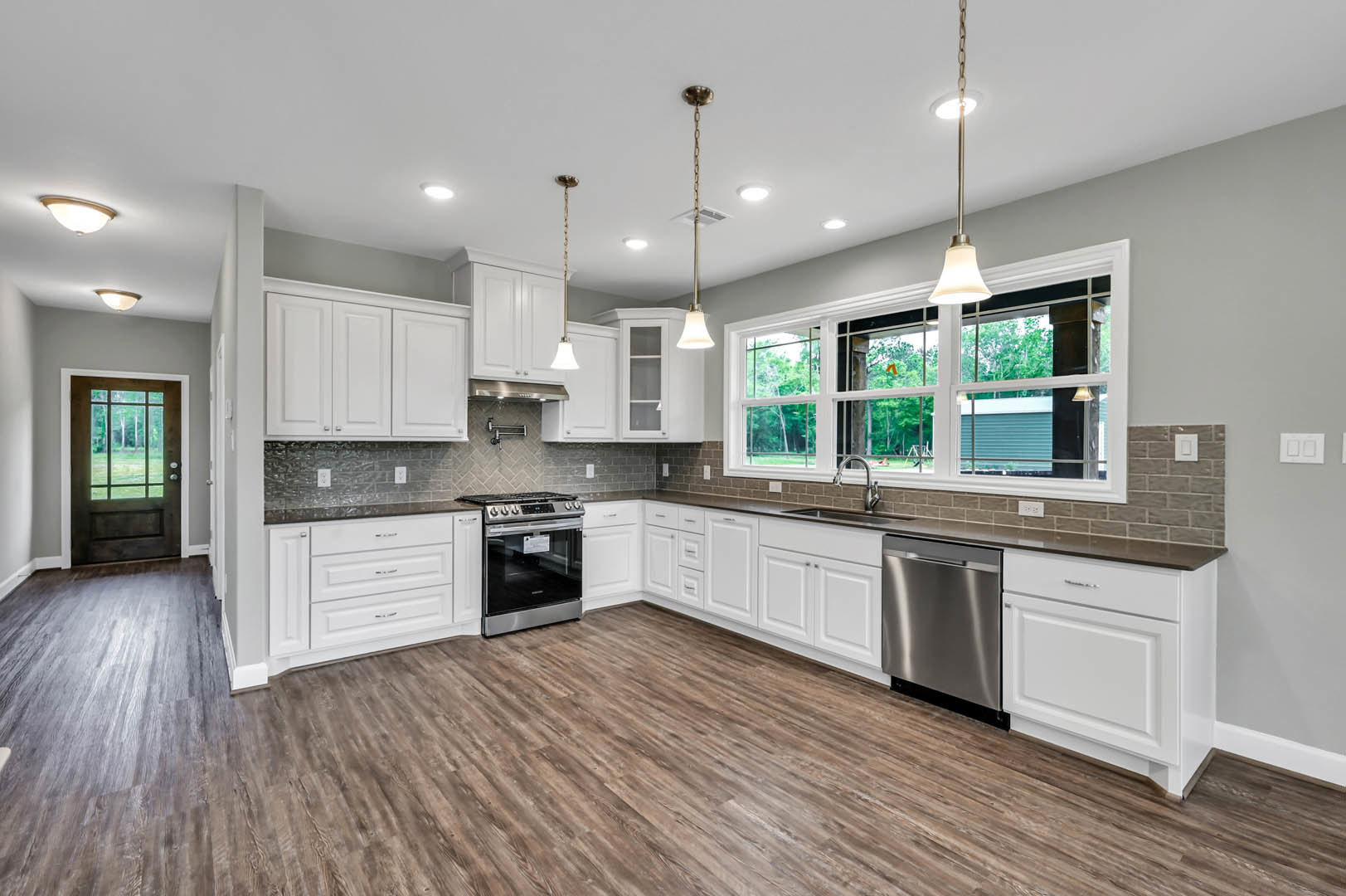 White kitchen cabinets, wood flooring, stainless steel dishwasher, glass door stove, double sinks, door with outdoor view