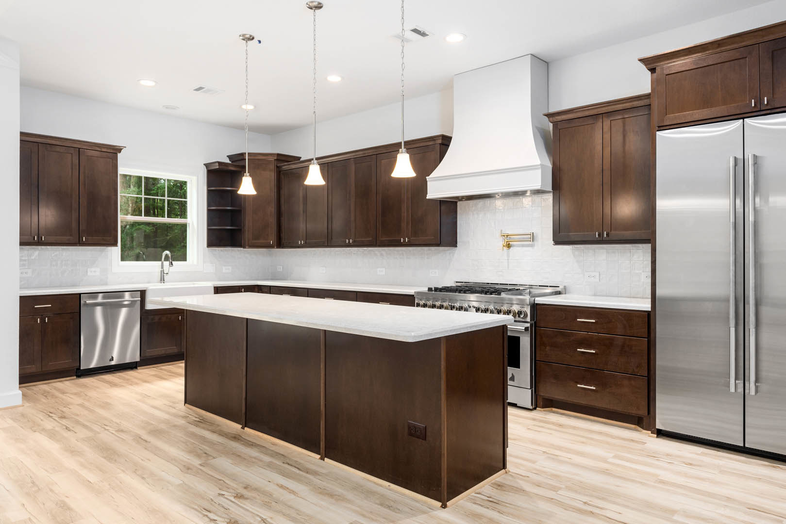 Dark wood kitchen cabinets, white quartz countertops, stainless steel dishwasher, refrigerator, undermount sink beneath a window, modern faucet, and sleek drawer fronts