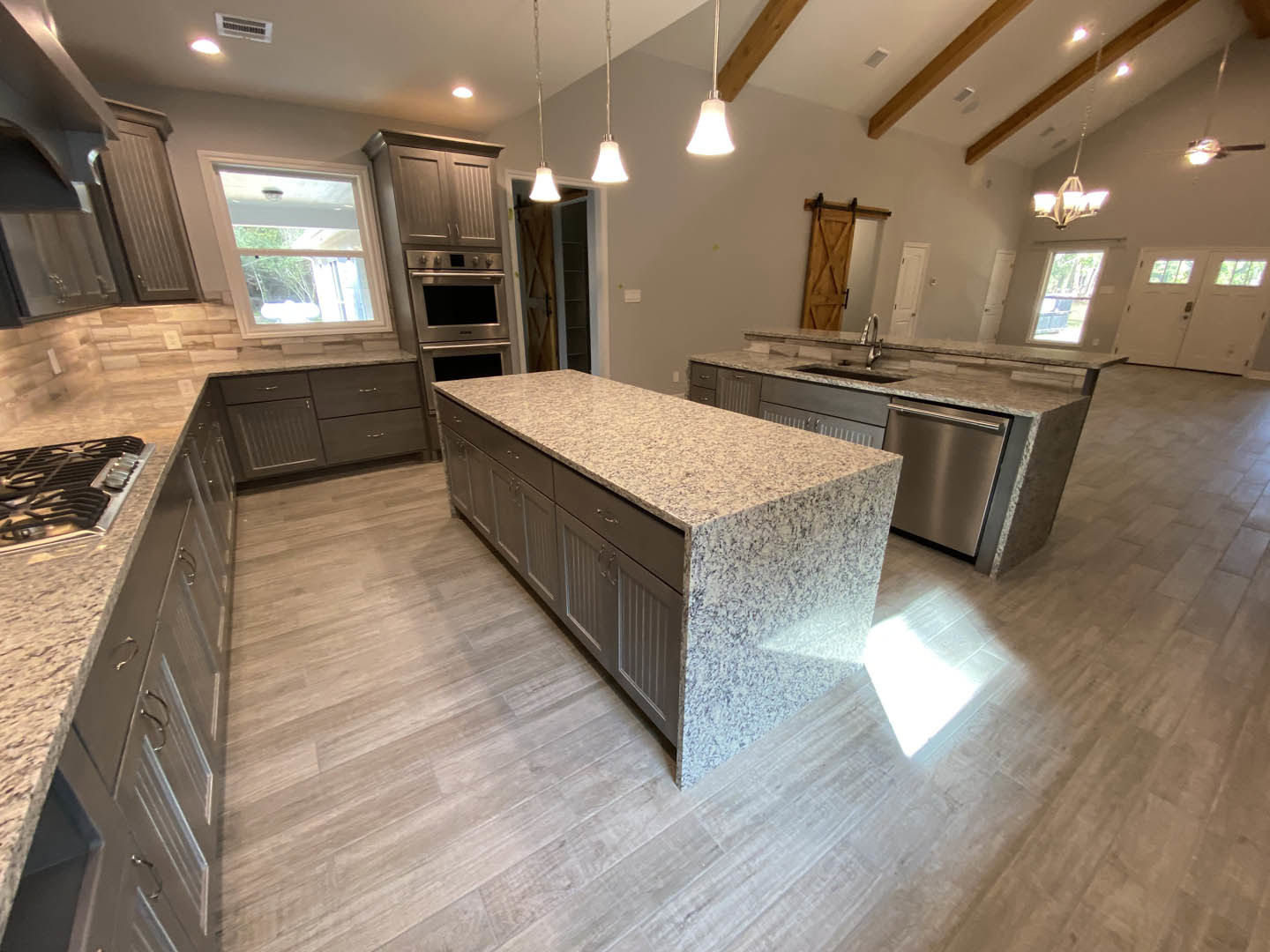 Spacious kitchen featuring a granite island, stainless steel appliances, white tile flooring, white-framed window, and modern cabinetry