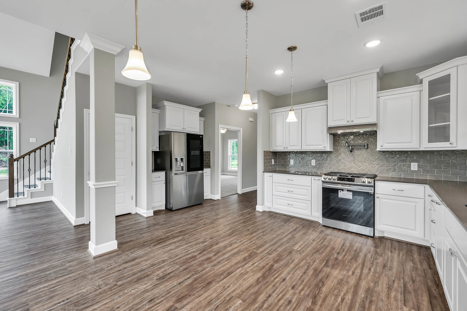 White kitchen cabinets with brushed nickel hardware, wood plank flooring, stainless steel refrigerator with water dispenser, gas stove, quartz countertops, pendant light fixture