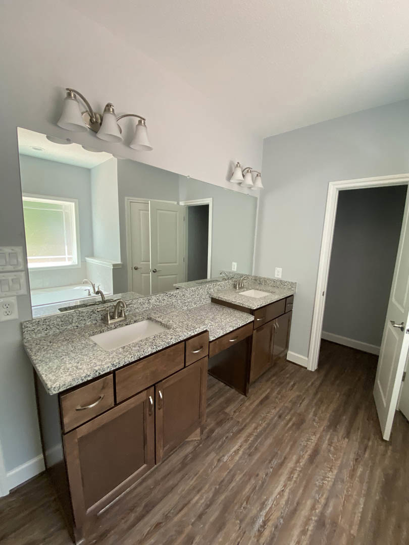 Bathroom with two undermount sinks set in a stone countertop, wide framed mirror above, tile flooring, white cabinetry, and chrome fixtures