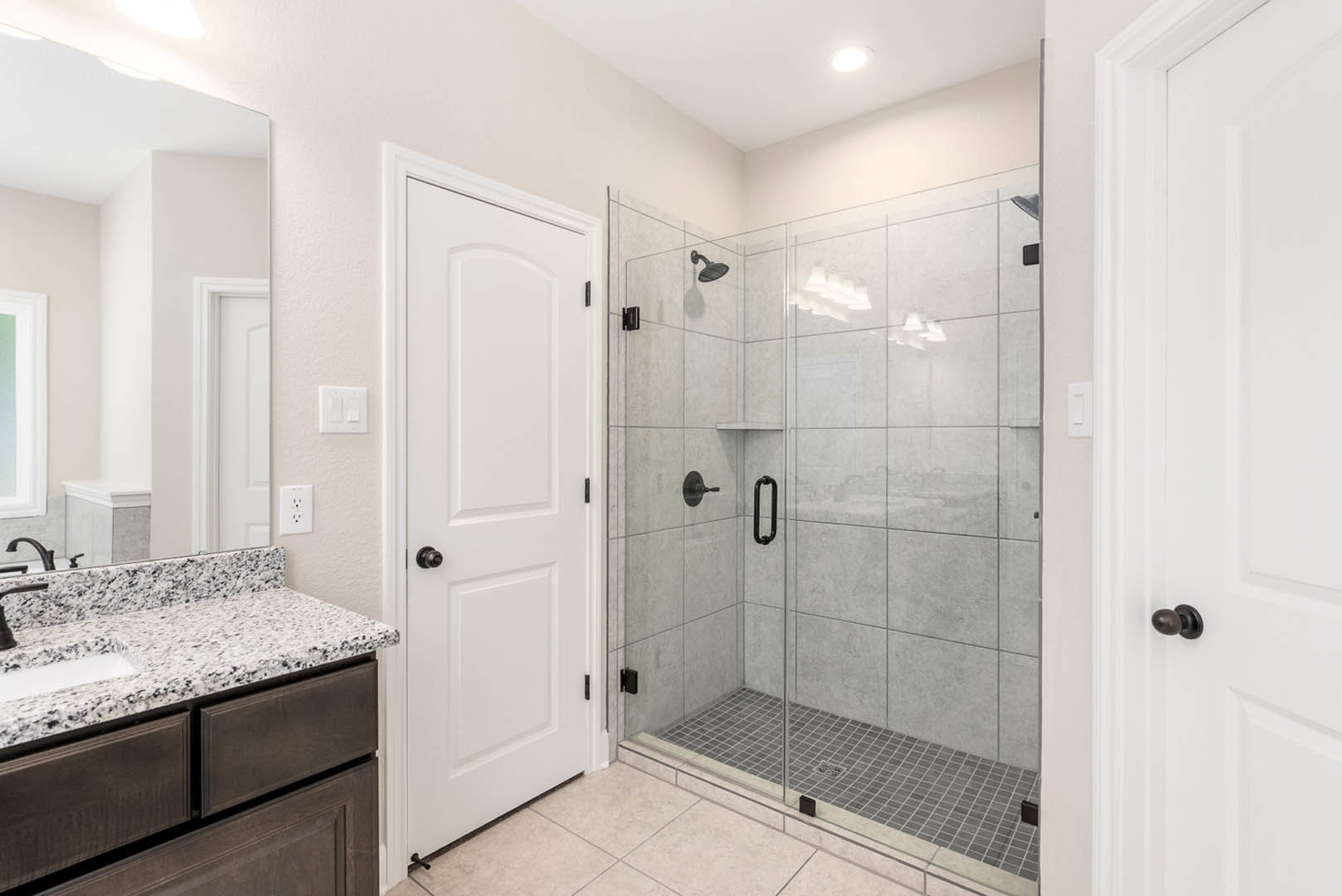 Bathroom featuring a glass shower enclosure, white door with black handle, light-colored countertop with built-in sink, white light switch on wall, and neutral cabinetry.
