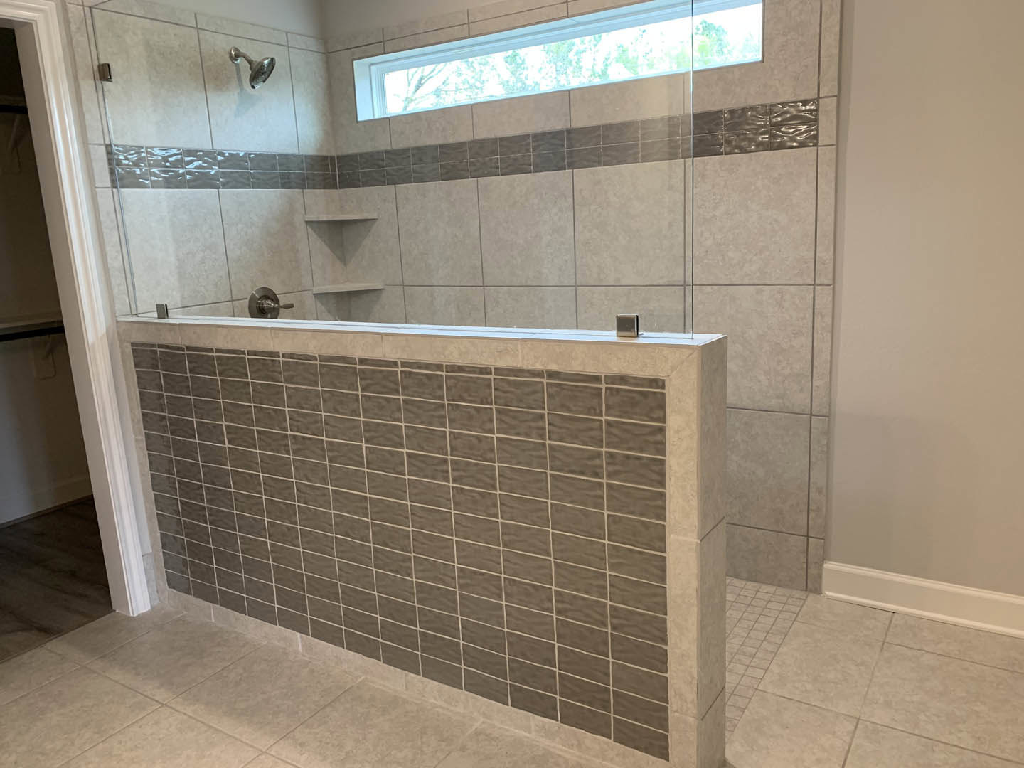 Shower with large rectangular window, marble tile walls, chrome shower head, white tile trim