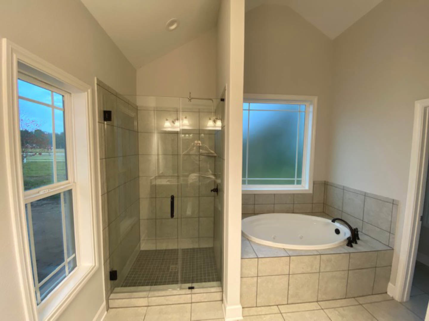 White freestanding bathtub beside glass-enclosed shower, gray tile walls, chrome fixtures, large window with natural light