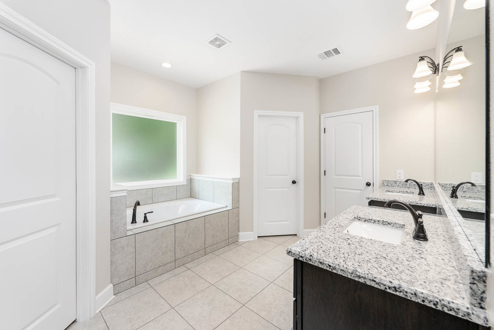 Bathroom with marble countertops, built-in tub, white cabinetry, chrome faucet, window overlooking greenery, ceiling light fixture, white door with black knob