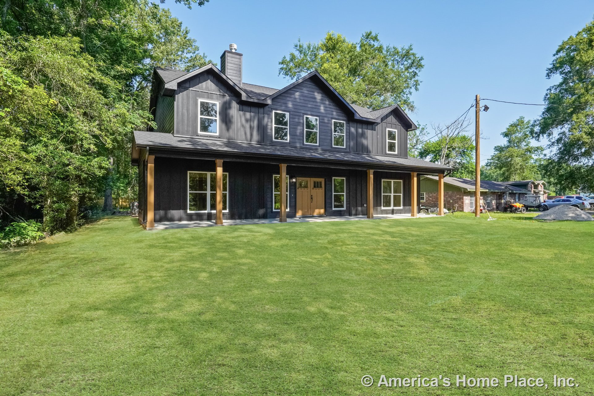 Dark board-and-batten siding with a covered front porch supported by wood columns, multiple large windows, double front doors, gabled roof, chimney, and contrasting trim on the