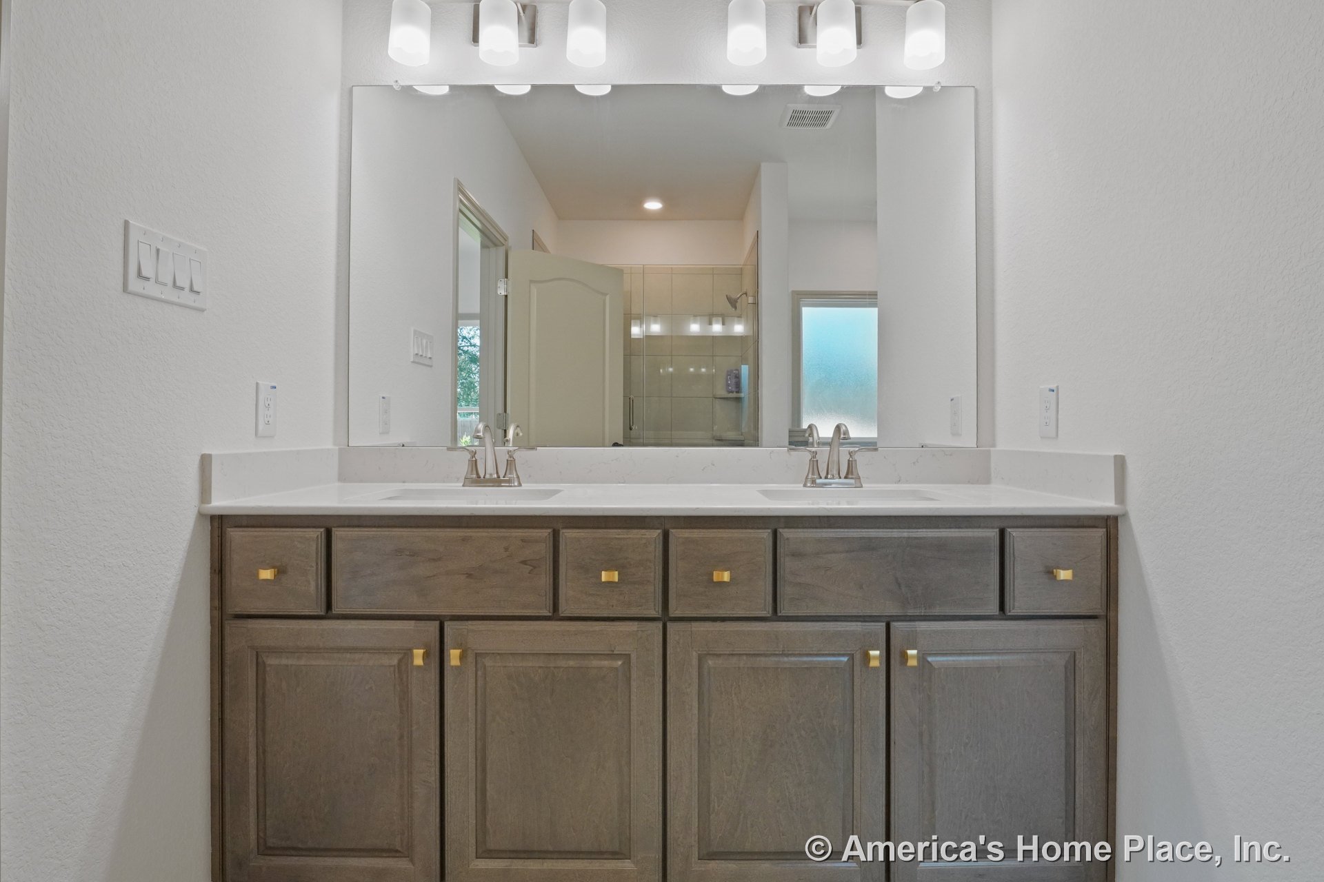 Double vanity with wood cabinets and brass hardware, quartz countertop with undermount sinks, expansive wall-mounted mirror, built-in vanity lighting, walk-in tile shower in