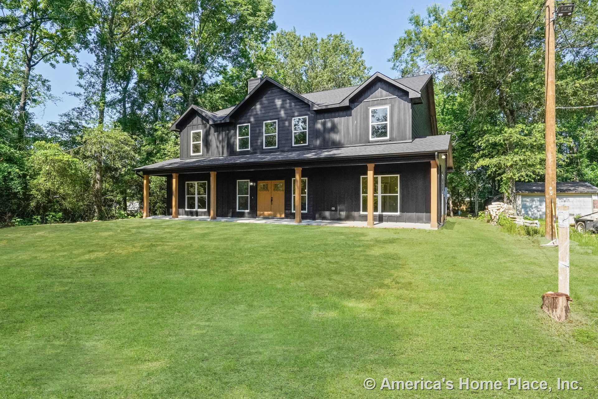 Two-story custom home with black wood siding, multiple rectangular windows, full-length covered front porch supported by wooden columns, double front doors, and contrasting trim