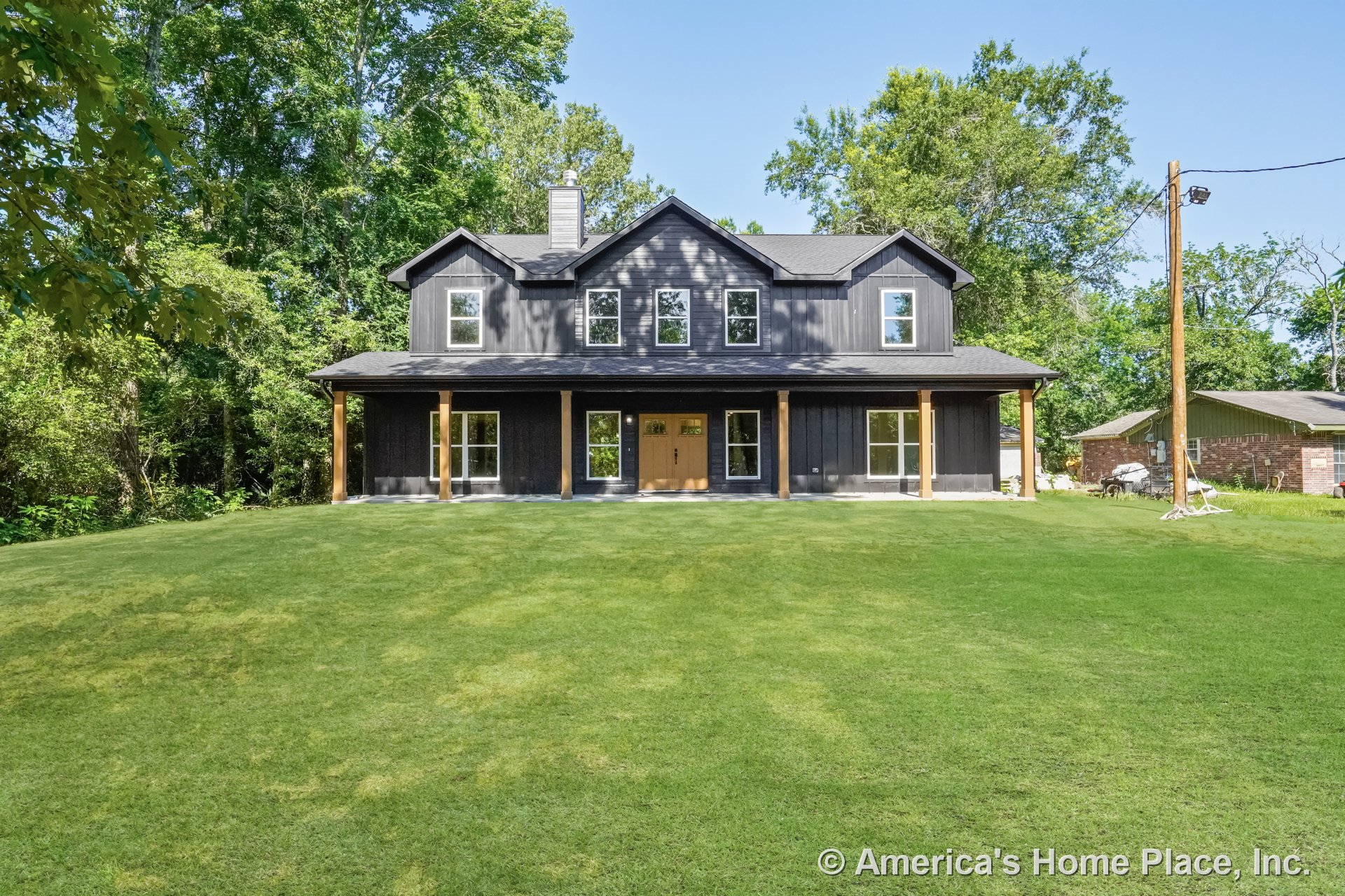 Dark board-and-batten siding with contrasting trim, covered front porch supported by wood columns, multiple double-hung windows, central double entry door, and prominent gabled