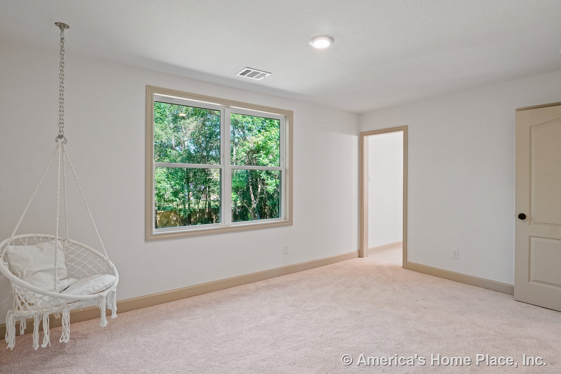 Bedroom with large double window framed by beige trim and baseboards, carpeted floor, recessed ceiling light, paneled door, and suspended swing chair fixture.