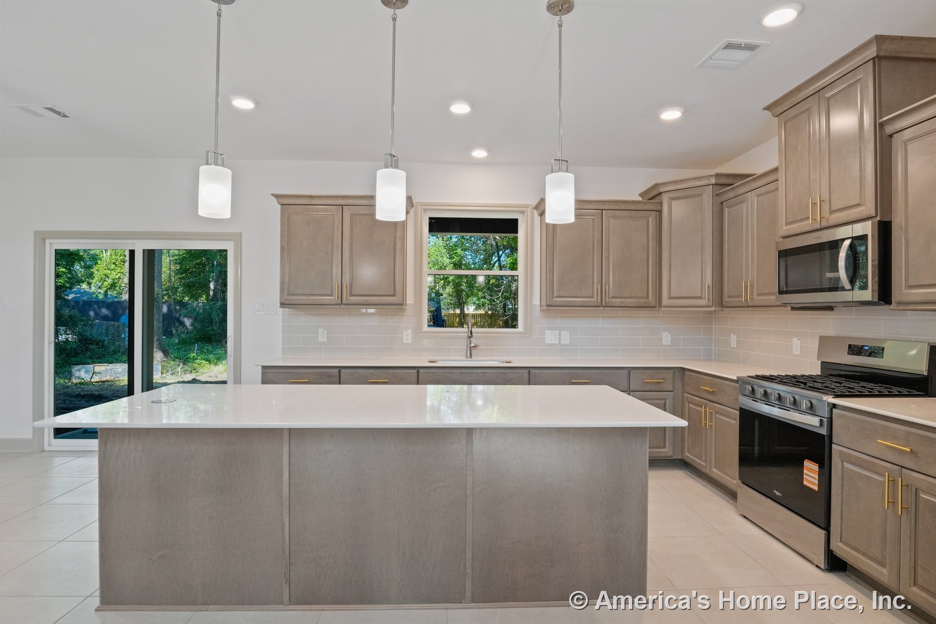 Light wood kitchen cabinets, large central island with quartz countertop, stainless steel appliances including gas range and microwave, pendant lighting fixtures above island