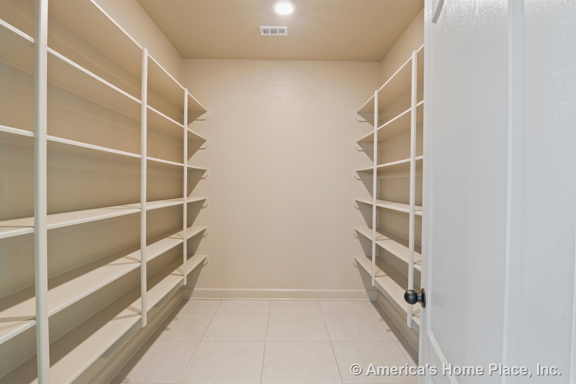 Walk-in pantry with built-in open shelving on both walls, tile flooring, recessed ceiling light, neutral painted walls, white trim, and ceiling vent.