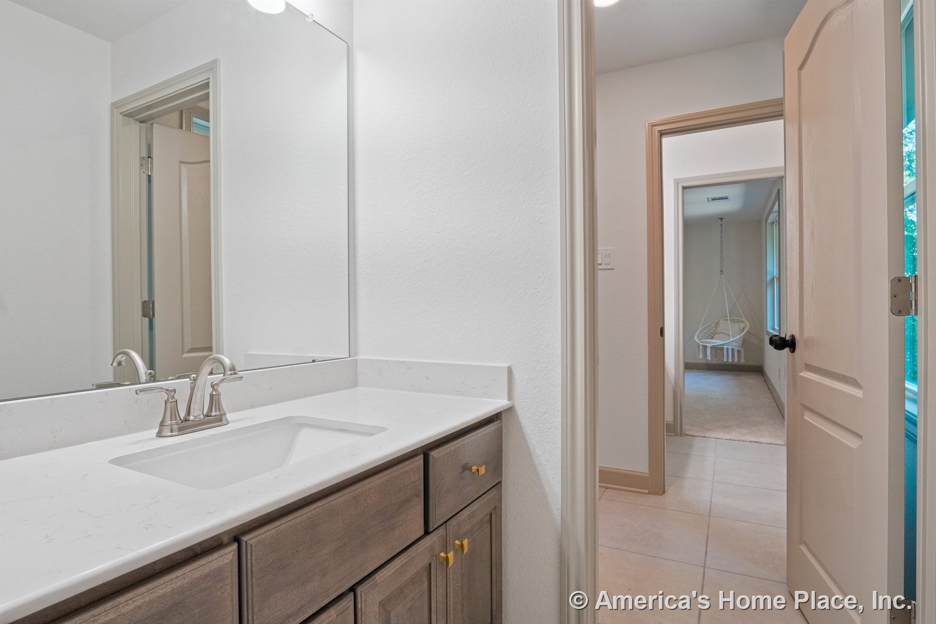 Quartz countertop with undermount sink atop wood cabinetry, large wall mirror above brushed nickel faucet, tile flooring, painted trim and doors, recessed ceiling light, doorway