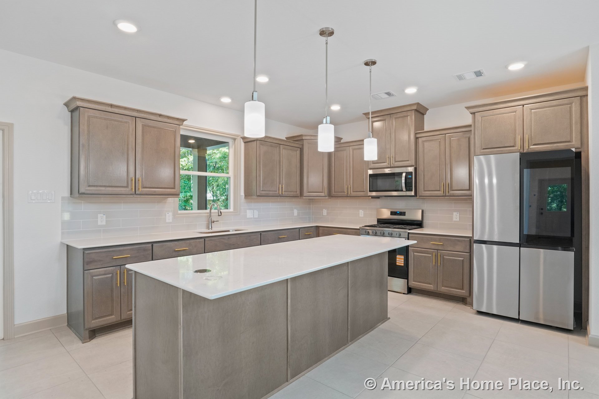 Light wood kitchen cabinetry with brushed gold hardware, large quartz island, stainless steel gas range and built-in microwave, subway tile backsplash, double window above sink