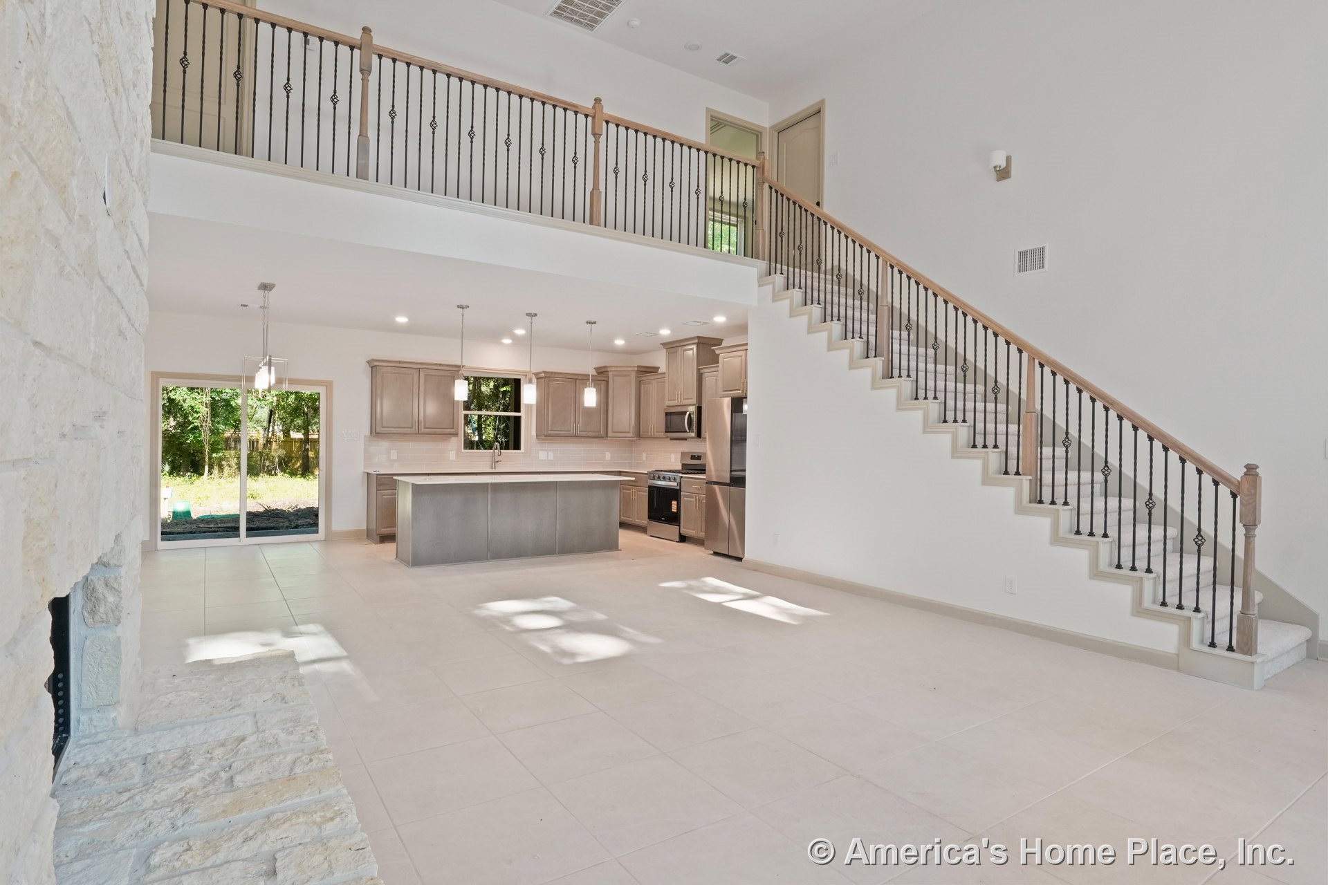 Open-concept living area with stone fireplace surround, large tile flooring, wood and iron staircase railing, pendant lighting above kitchen island, built-in cabinetry, stainless