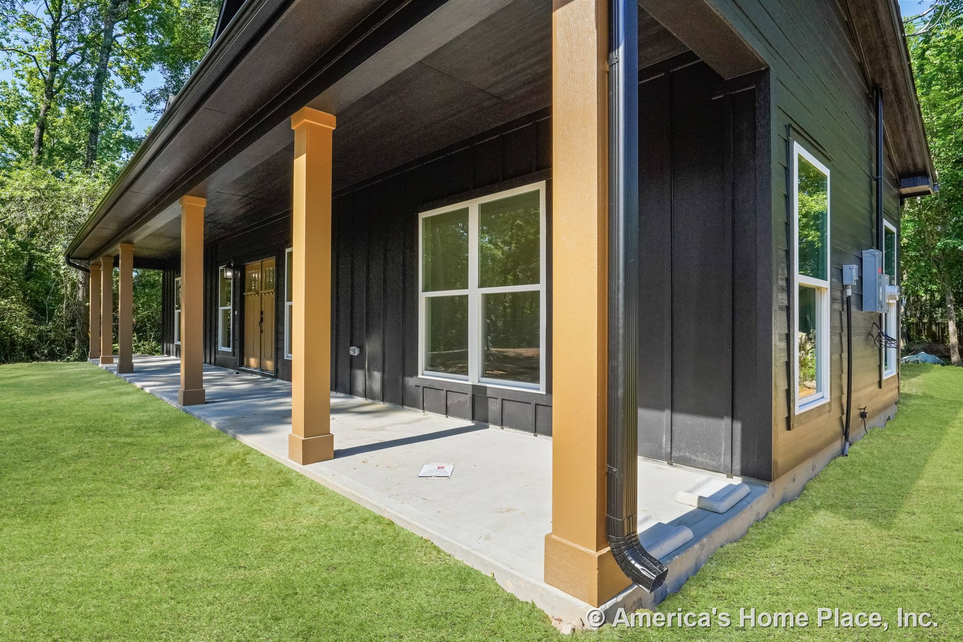 Covered front porch with concrete slab flooring, wood support columns, black vertical siding, large double-pane windows, and exterior door featuring glass panels.