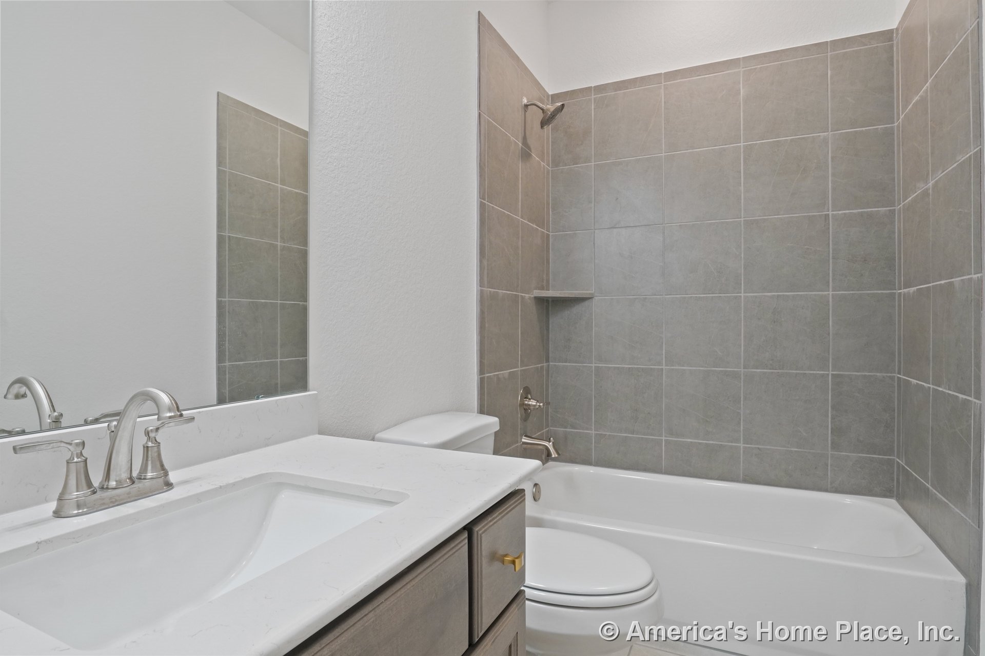 Gray tile shower surround, built-in bathtub, white quartz vanity top with under-mount sink, brushed nickel faucet, wood cabinetry, and neutral color palette.