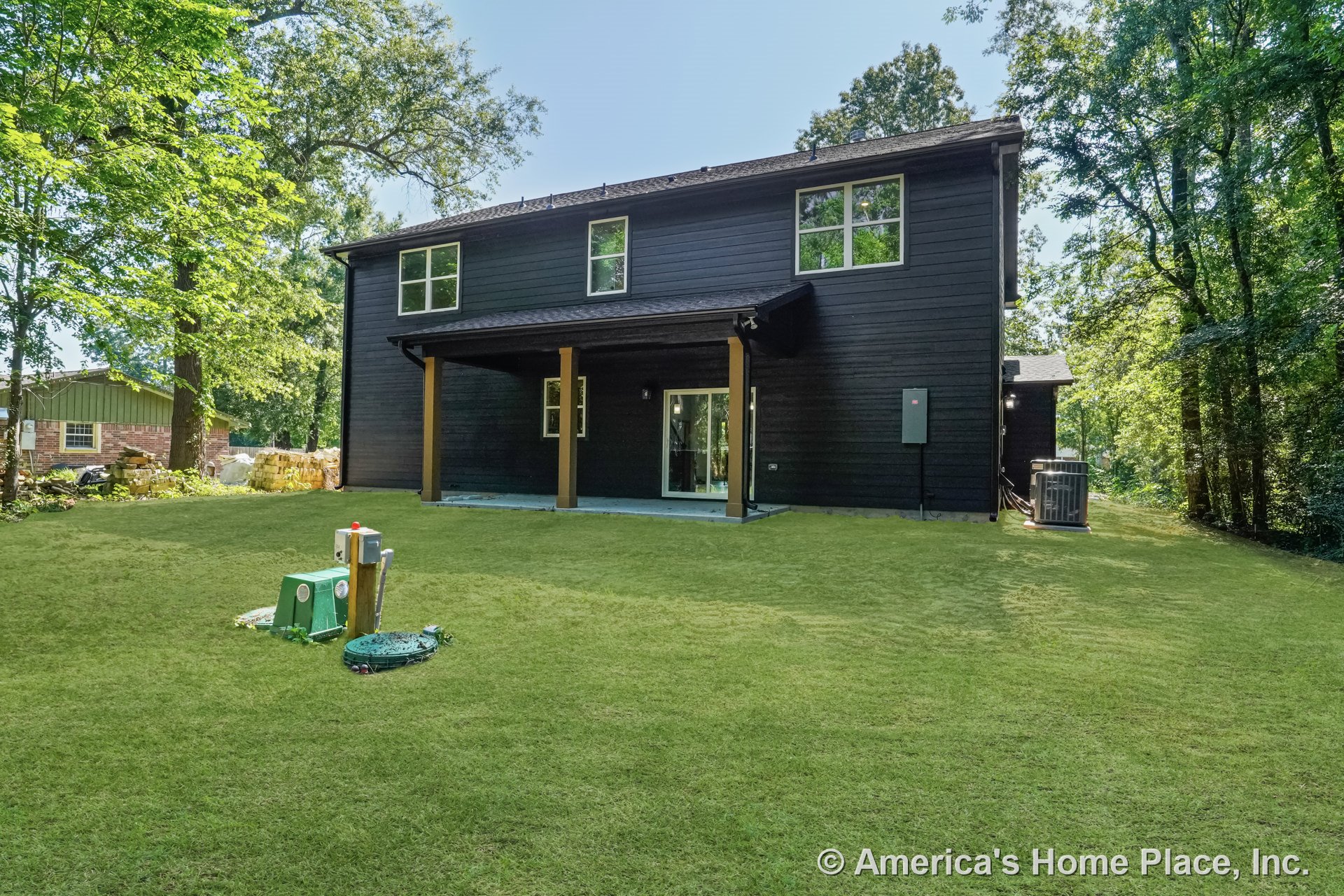 Dark wood siding two-story home with expansive windows, sloped roof, covered back patio supported by wooden posts, and concrete patio flooring.