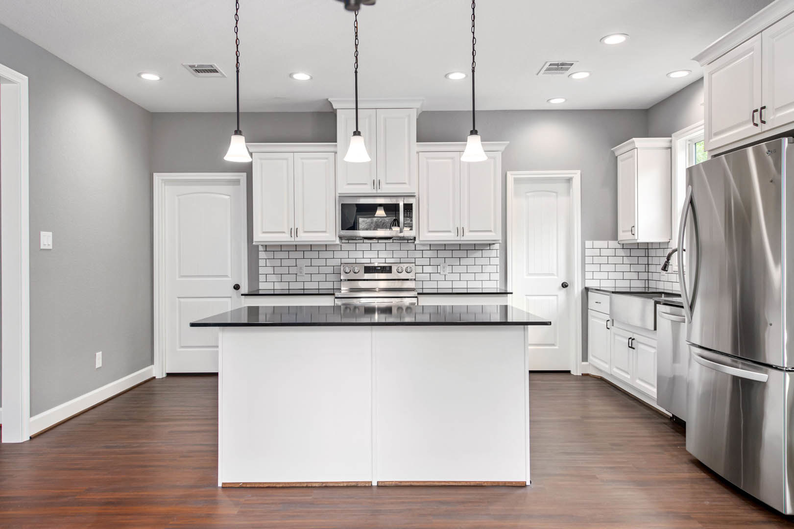 White kitchen cabinets with black countertops, stainless steel refrigerator, stove, white table with lamp, white board with black trim, chain hanging from pole