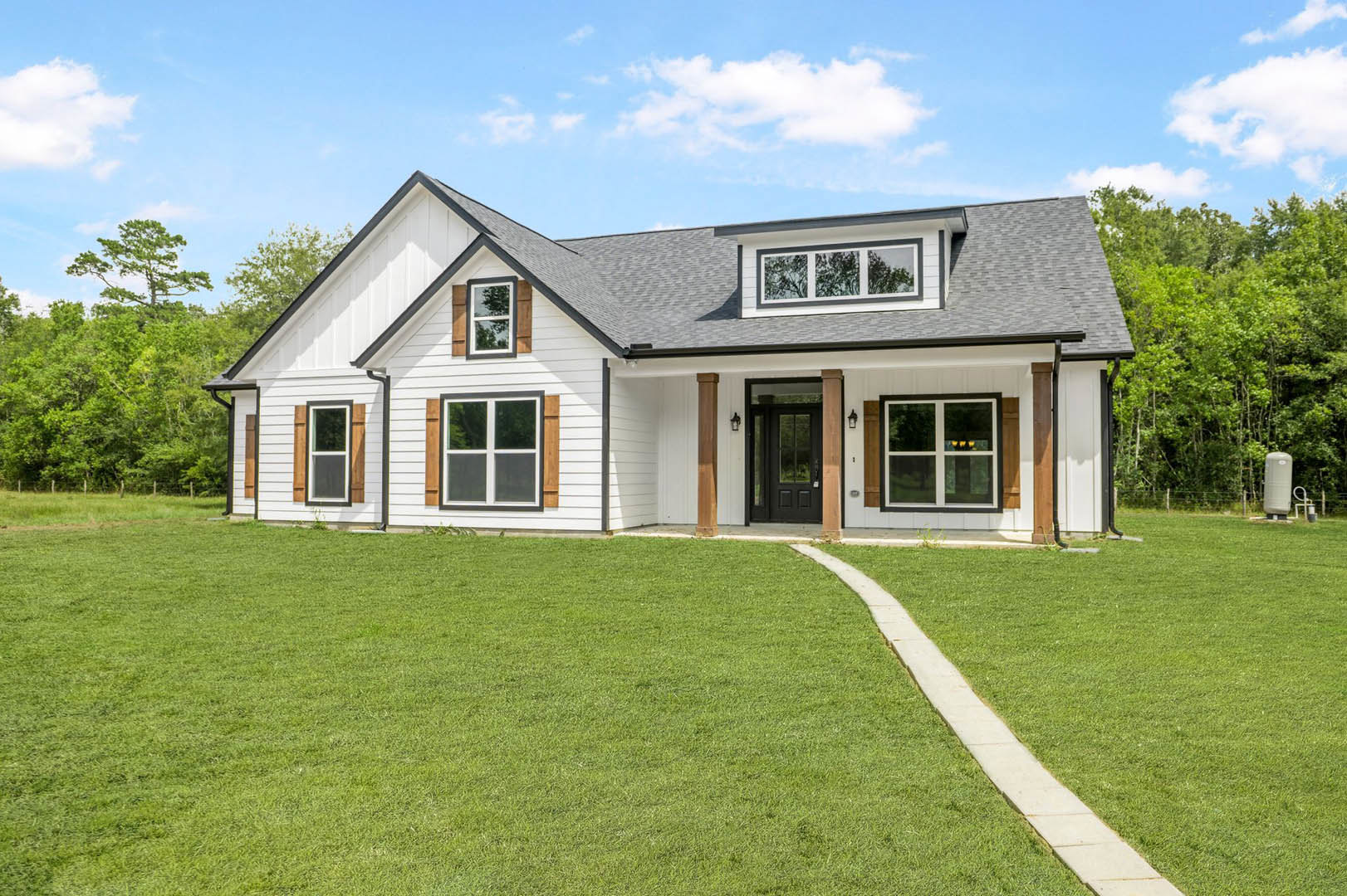 White house with black front door, brown porch pillars, white-framed windows, and long green grass lawn