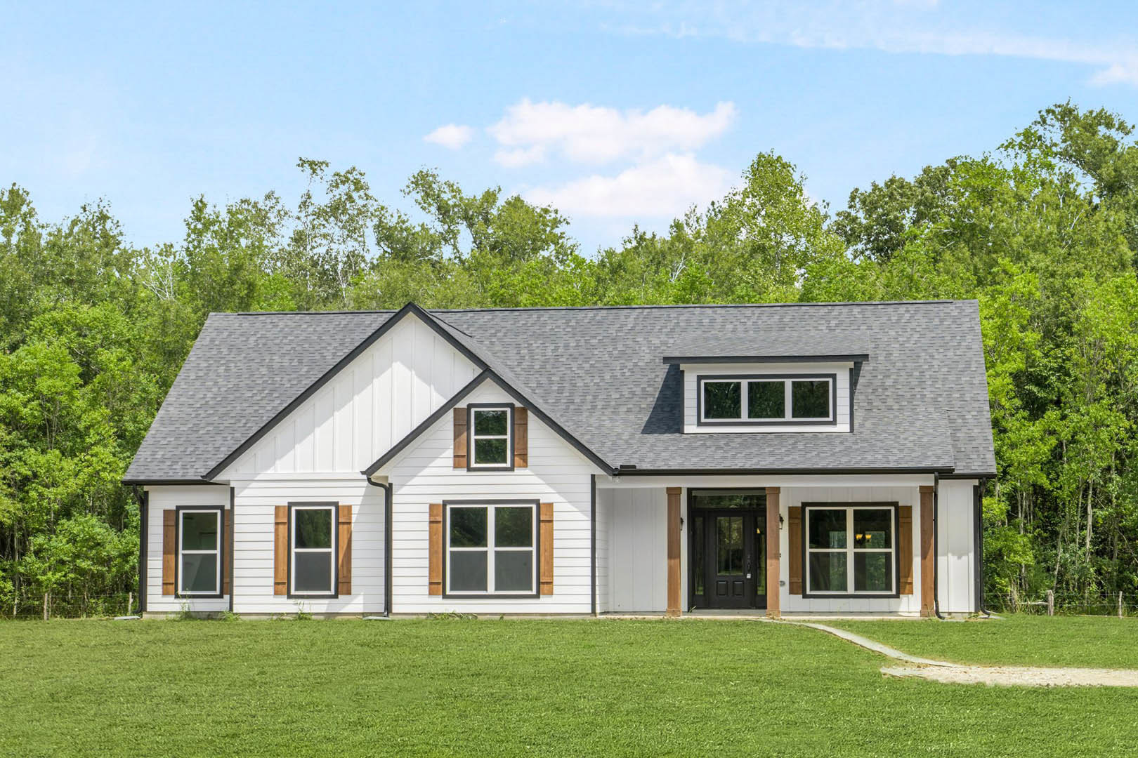 Two-story farmhouse with black roof, white-framed windows, black glass-paneled front door, manicured green lawn, and mature trees in the background