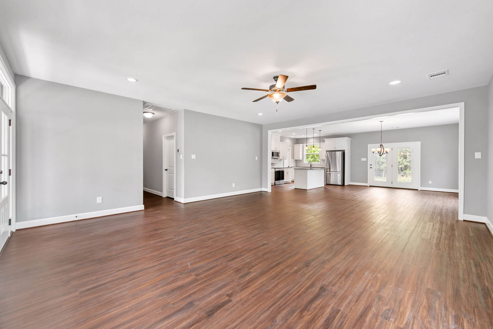 Spacious room with hardwood flooring, white walls, ceiling fan with light fixture, and glass-paneled door