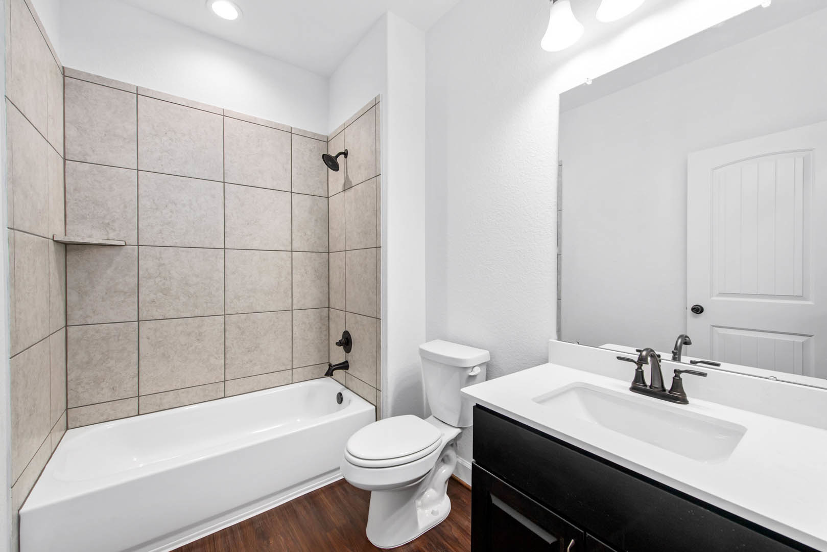 Bathroom with white toilet, freestanding bathtub, black cabinet sink, black shower head, and white door with curved top; light tile walls and floor.