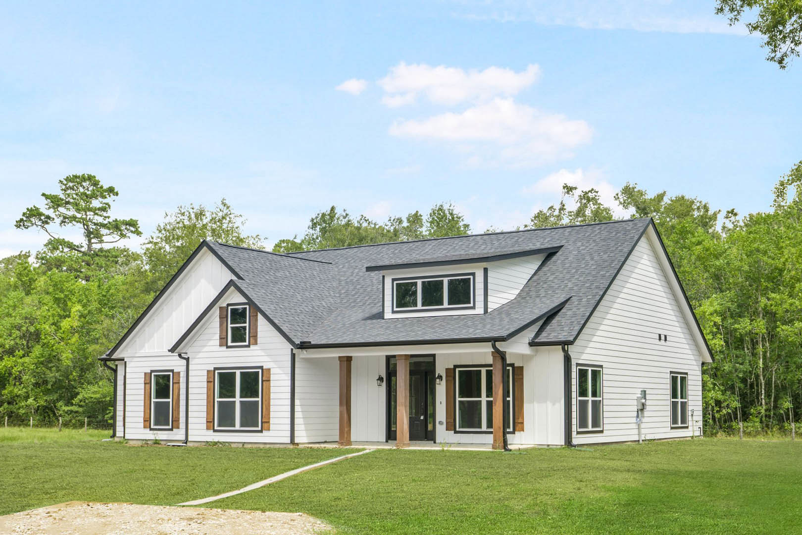 White house with black roof, white-framed windows, green lawn, and mature trees in the background