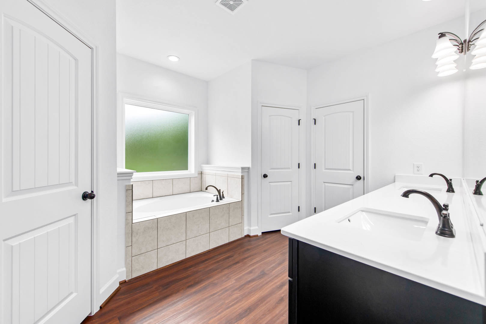 Modern bathroom featuring a freestanding bathtub, white sink with chrome faucets, frosted glass window, tiled walls, and a close-up of a contemporary lamp and white door