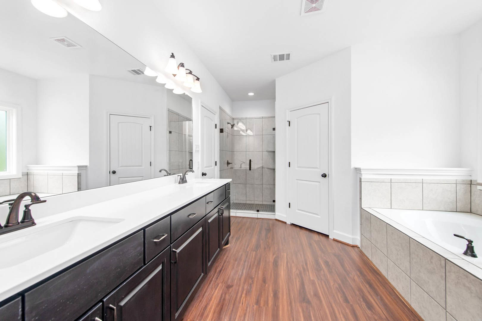 Bathroom with a white countertop and dark cabinets, large sink with chrome faucet, freestanding bathtub, wood floor with white trim, white cabinet featuring black handles