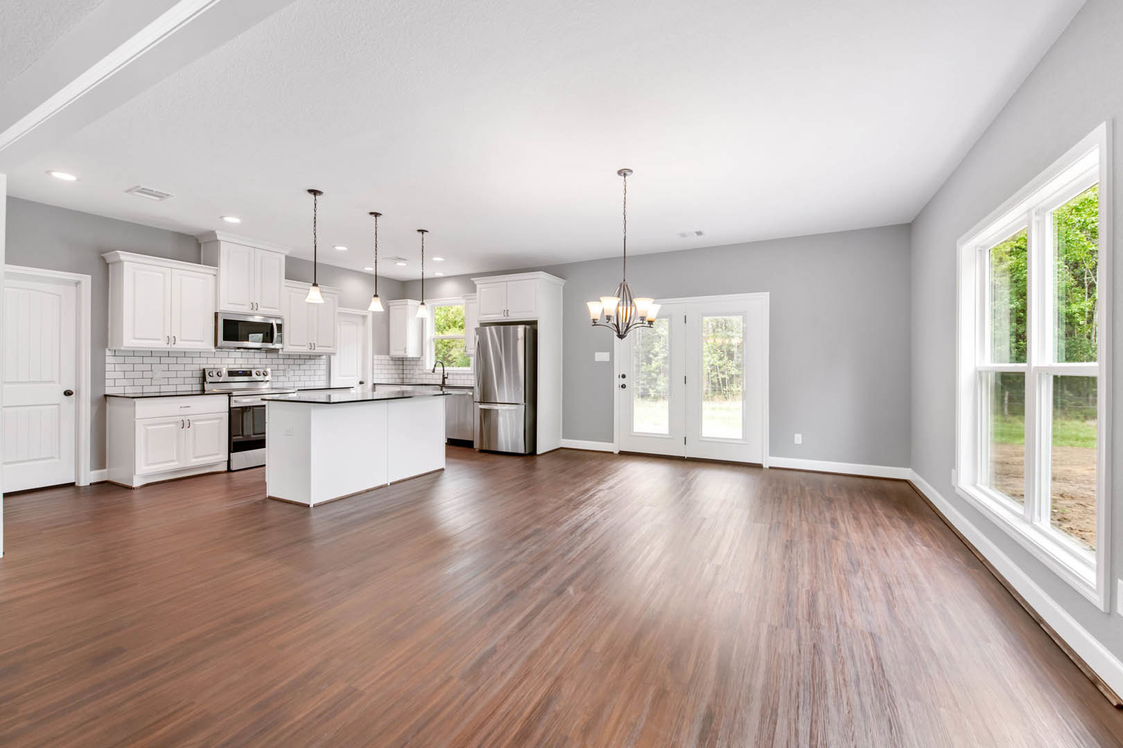 Open kitchen and dining area featuring hardwood flooring, white cabinetry with black countertops, stainless steel refrigerator, glass-door microwave, and a window providing natural