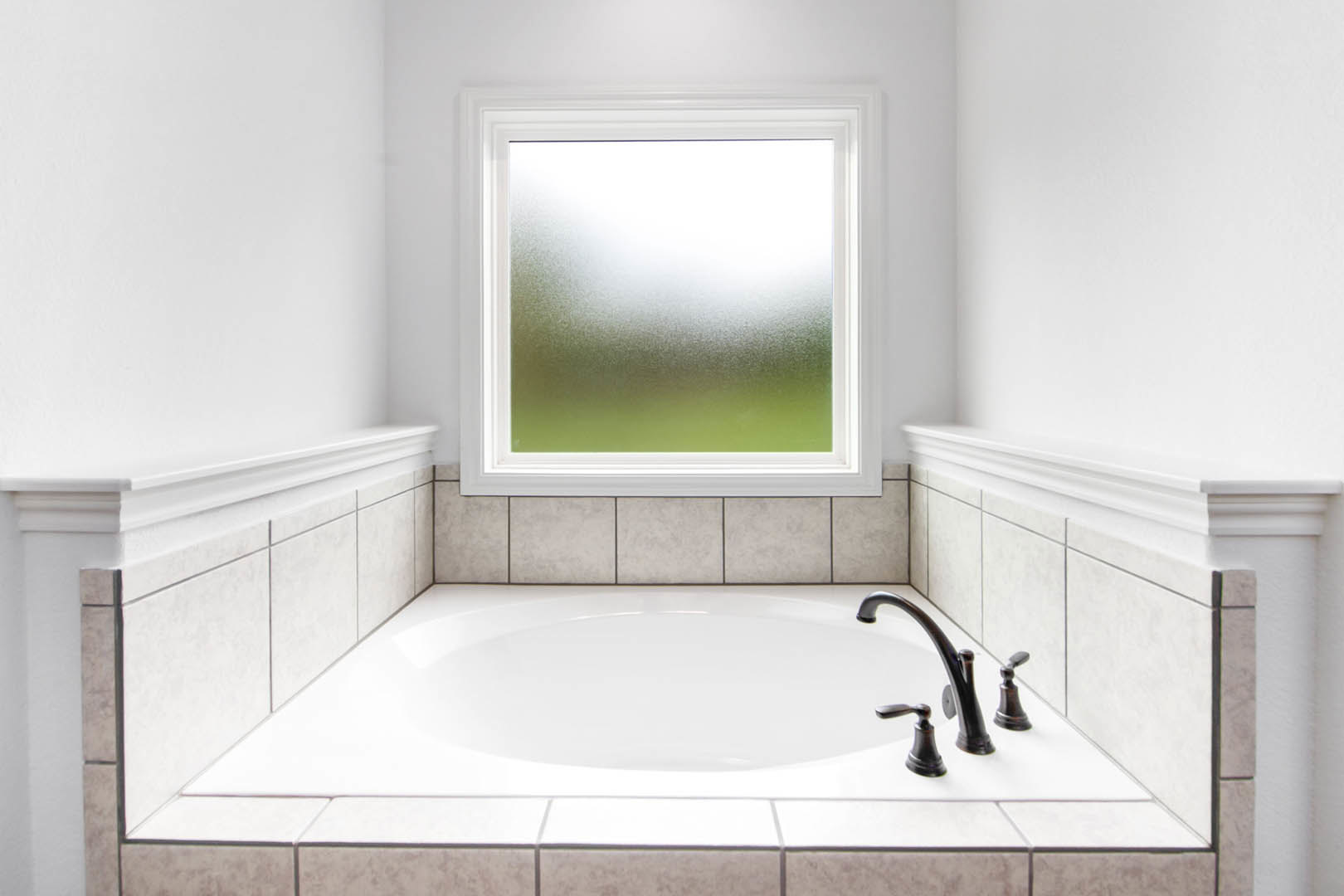 White freestanding bathtub beneath frosted glass window, chrome faucet, light tile walls