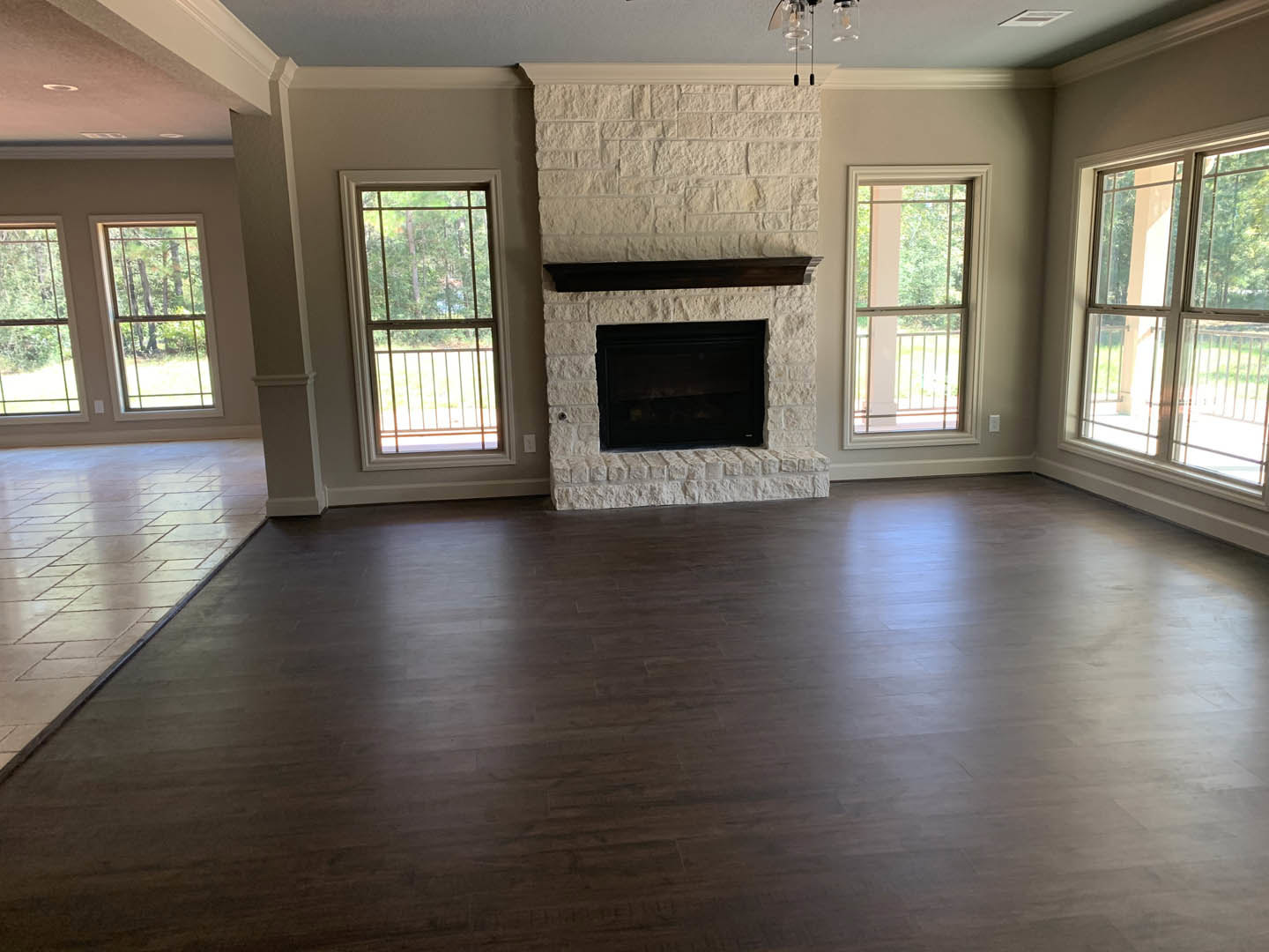 Black fireplace set against a white brick accent wall, hardwood flooring, large windows with metal railings, and leafy trees visible outside